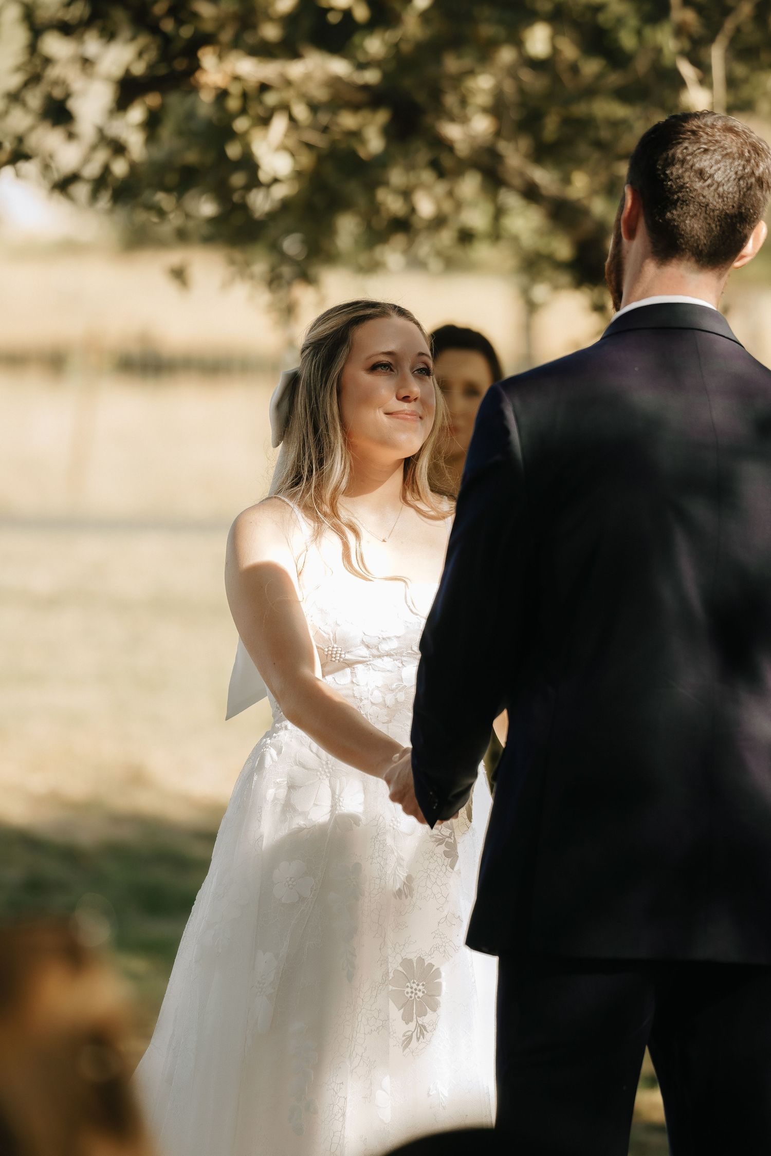 A romantic outdoor wedding scene with sunlight filtering through trees as couple shares a moment.