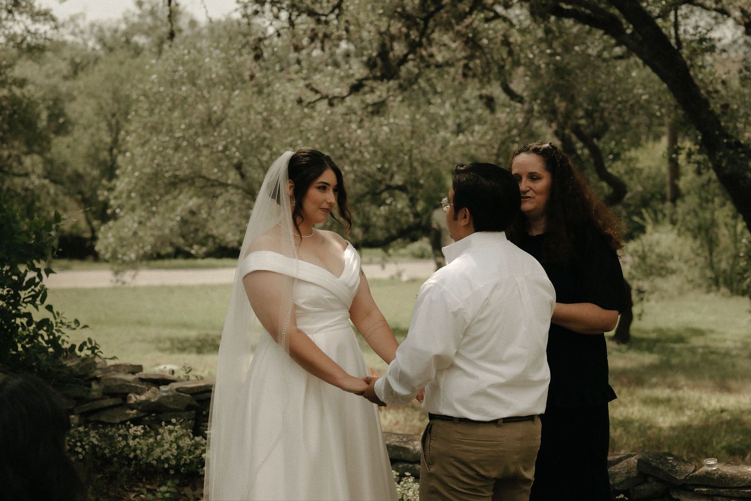 An intimate wedding ceremony takes place under a canopy of trees.