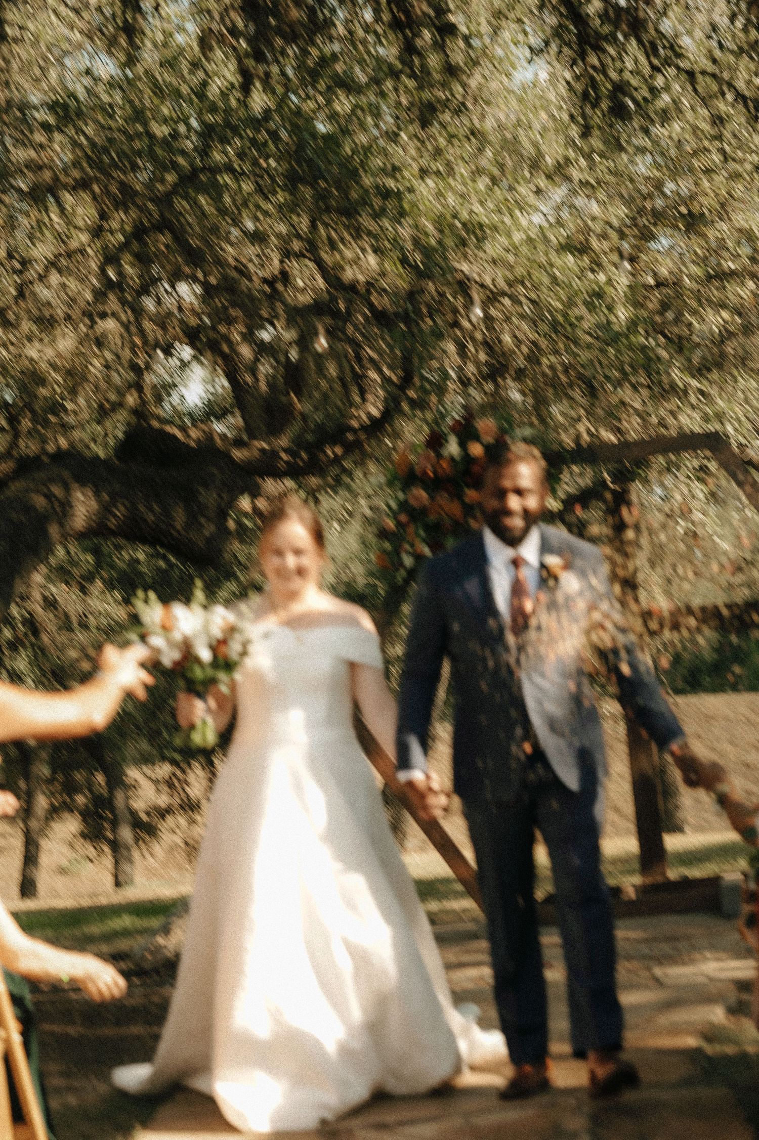 Wedding party members walk and celebrate on a tree-lined path during the ceremony.