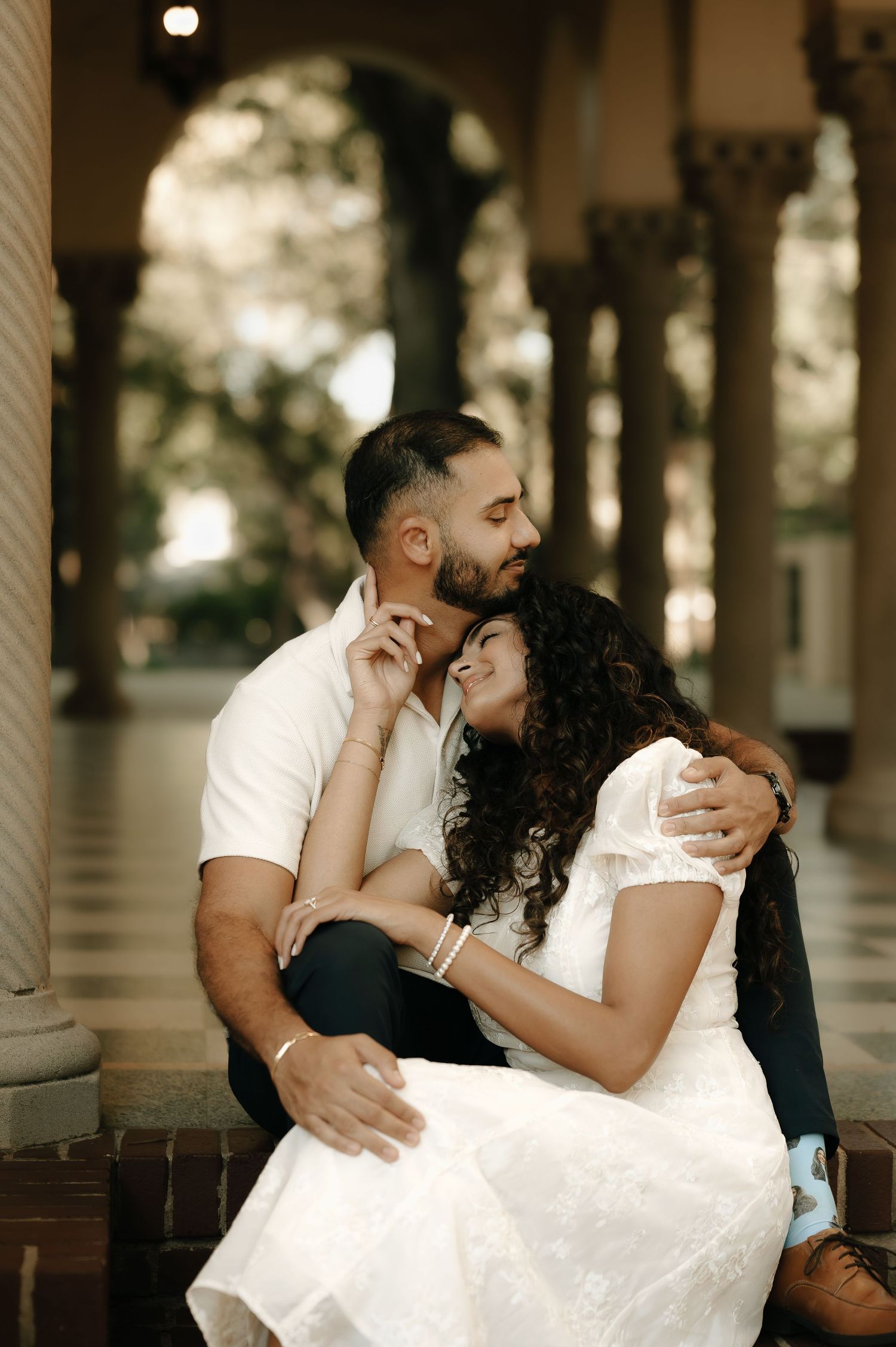 Couple embracing tenderly under a covered colonnade with soft lighting.