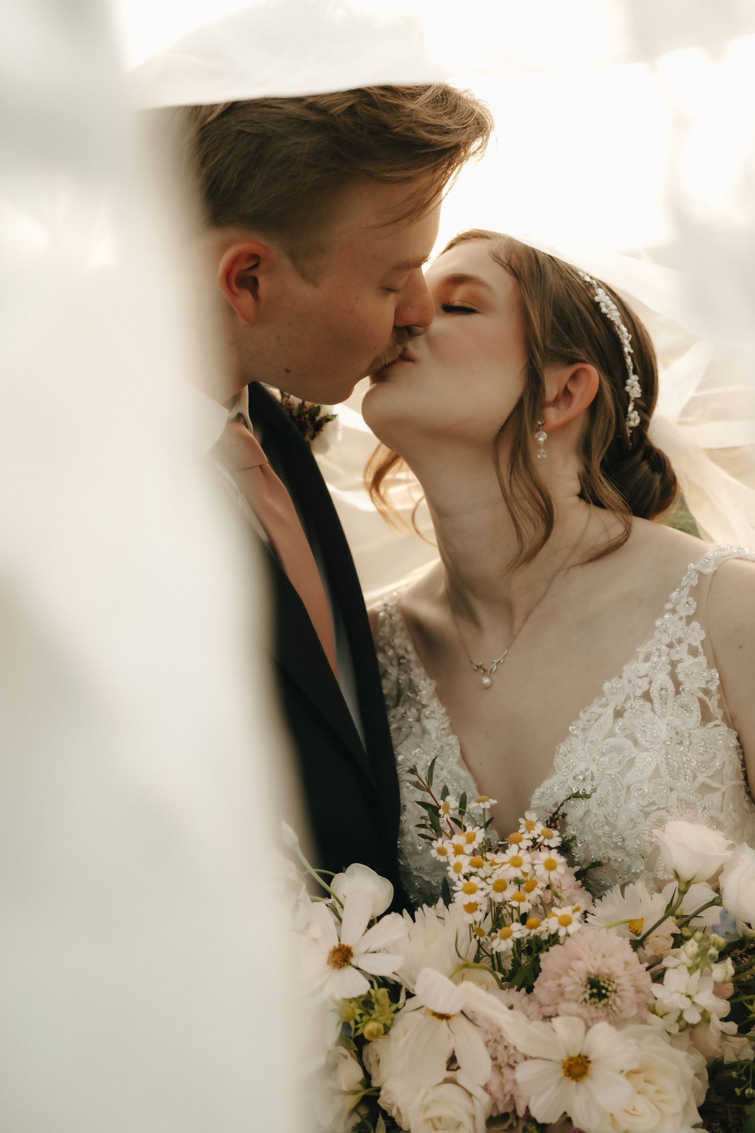 Romantic wedding portrait with couple holding white floral bouquet in soft light.