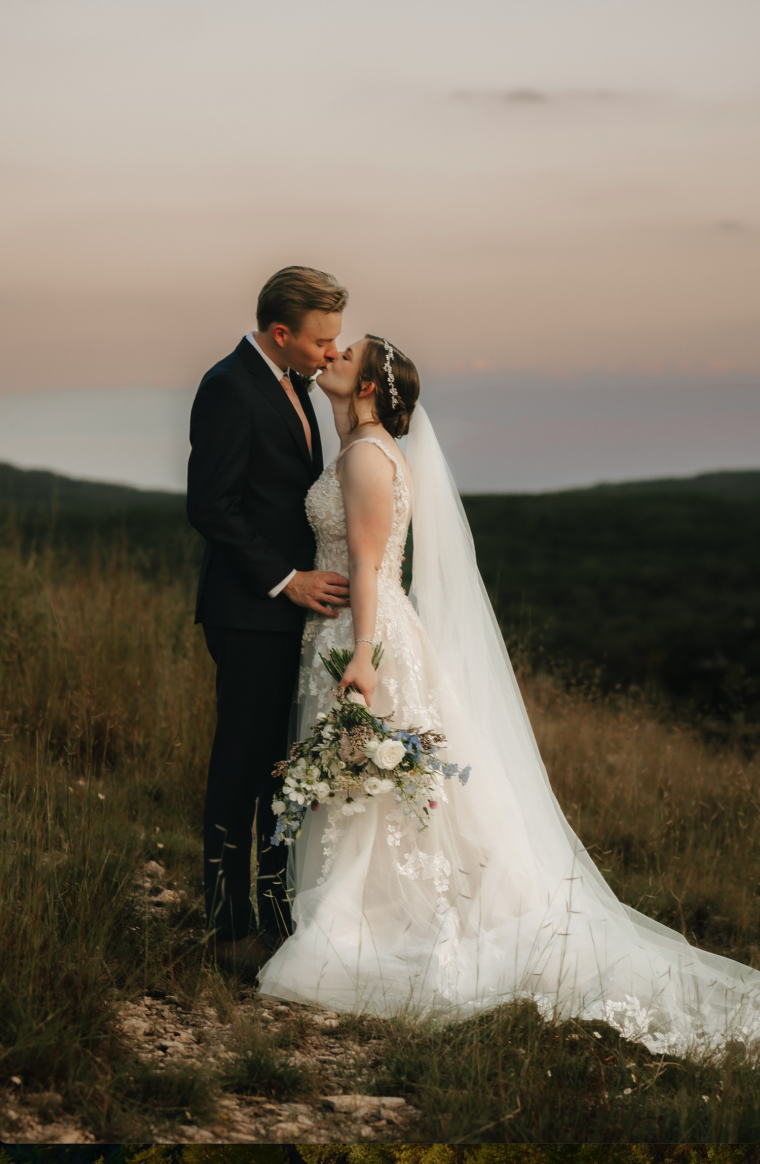Romantic sunset wedding portrait of a couple in a field with mountains in the background.