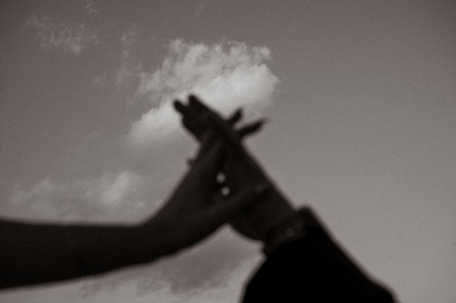 Silhouetted hands creating shapes against a bright cloudy sky.
