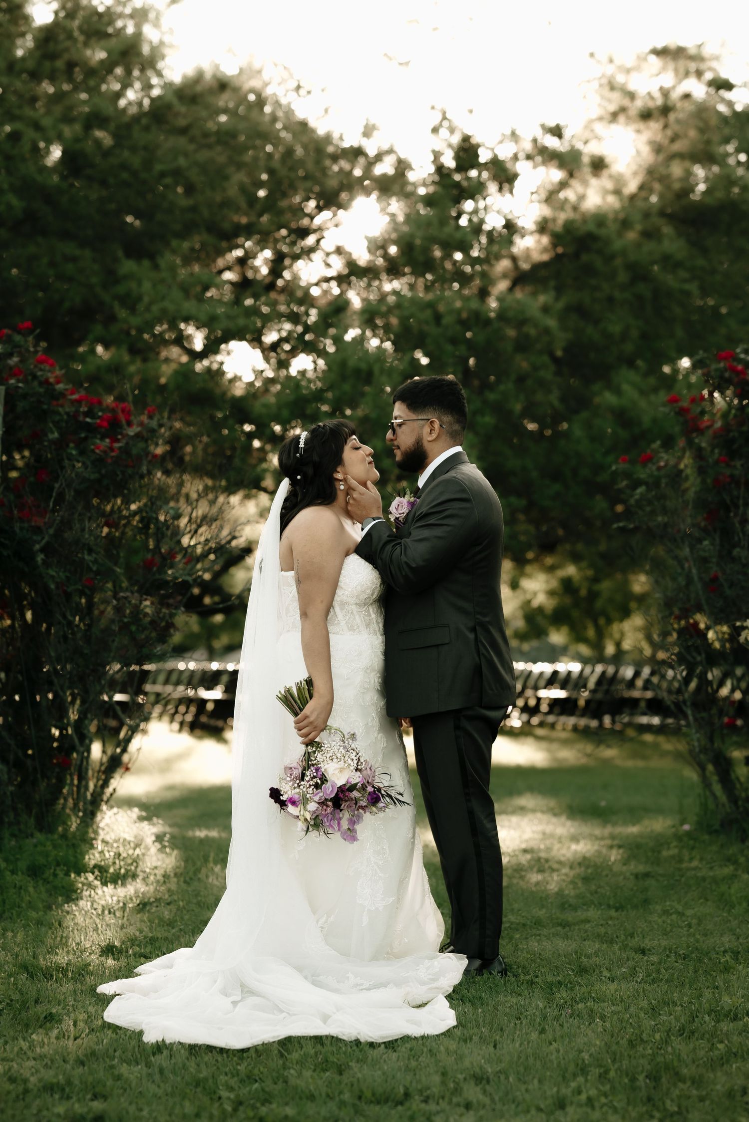 Romantic wedding portraits of a couple sitting in a garden with purple flowers at sunset.