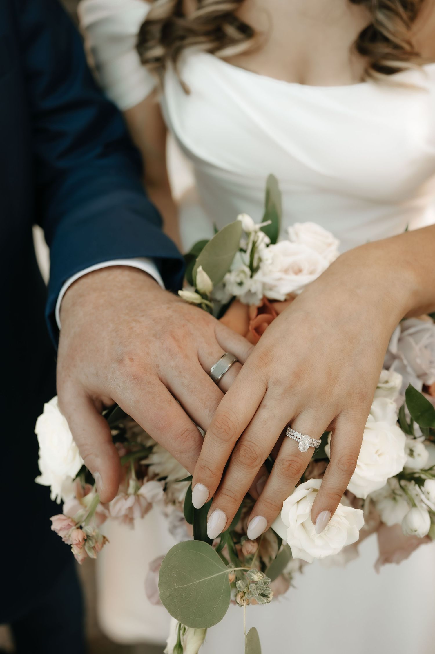 Close-up of hands with wedding rings surrounded by white floral decorations and greenery.
