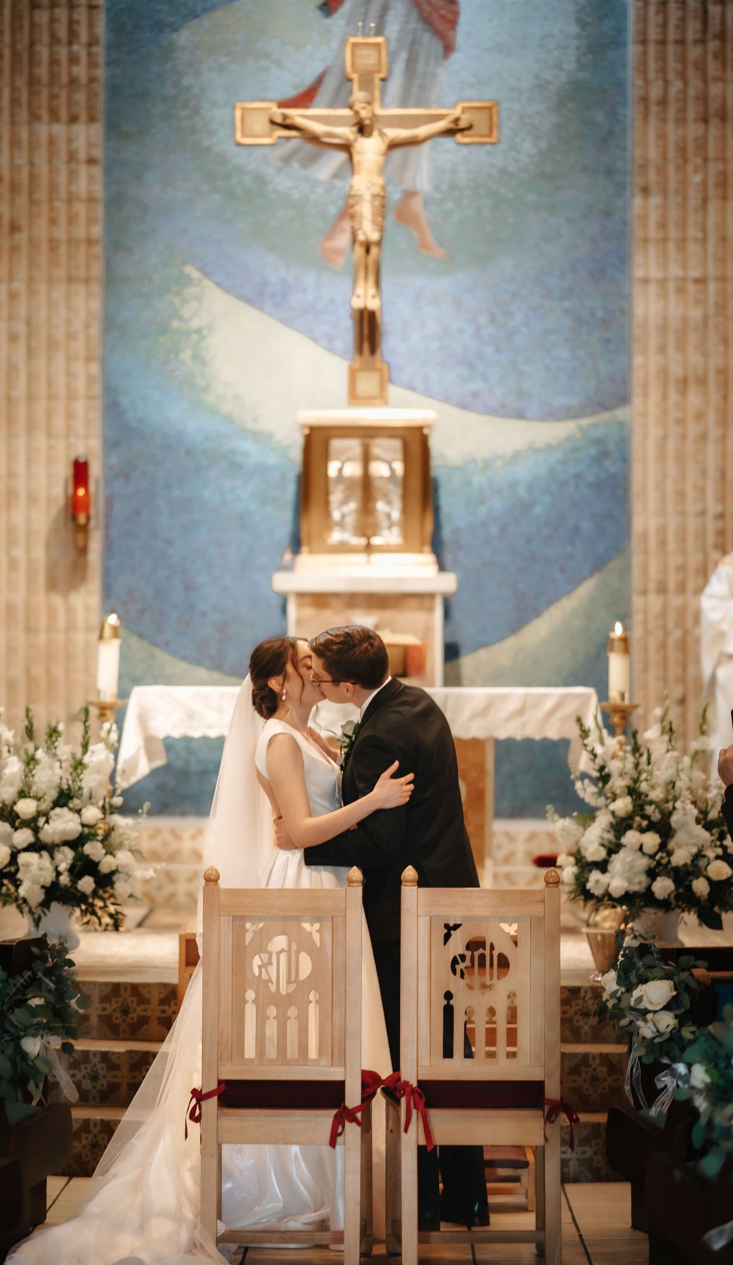 Romantic church wedding ceremony with crucifix altar and white floral arrangements framing the couple's first kiss.