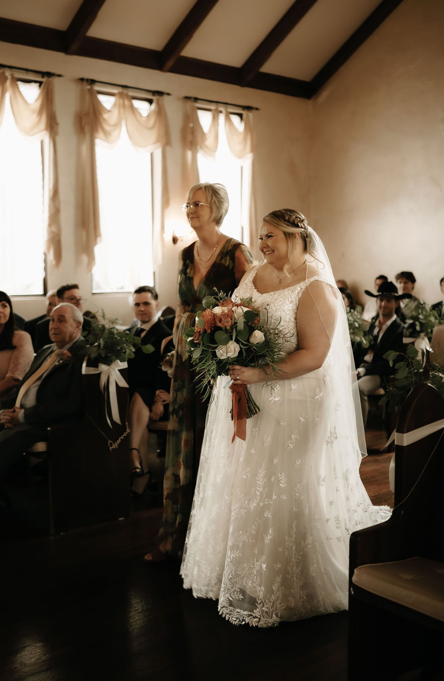 Wedding ceremony in rustic venue with exposed beams and elegant window treatments.