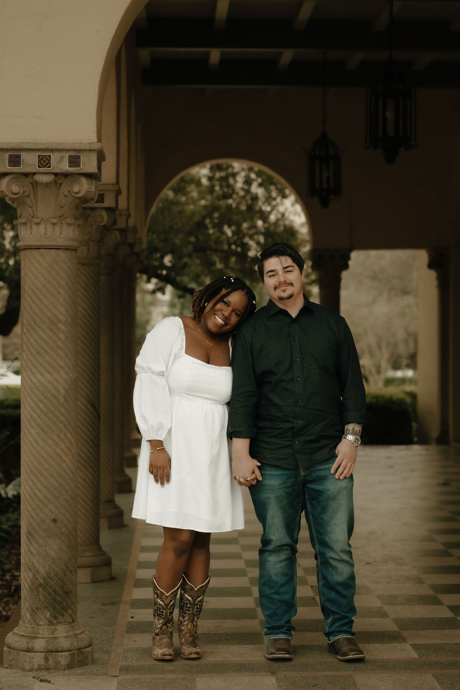 A couple laughs together while walking under an ornate columned archway.