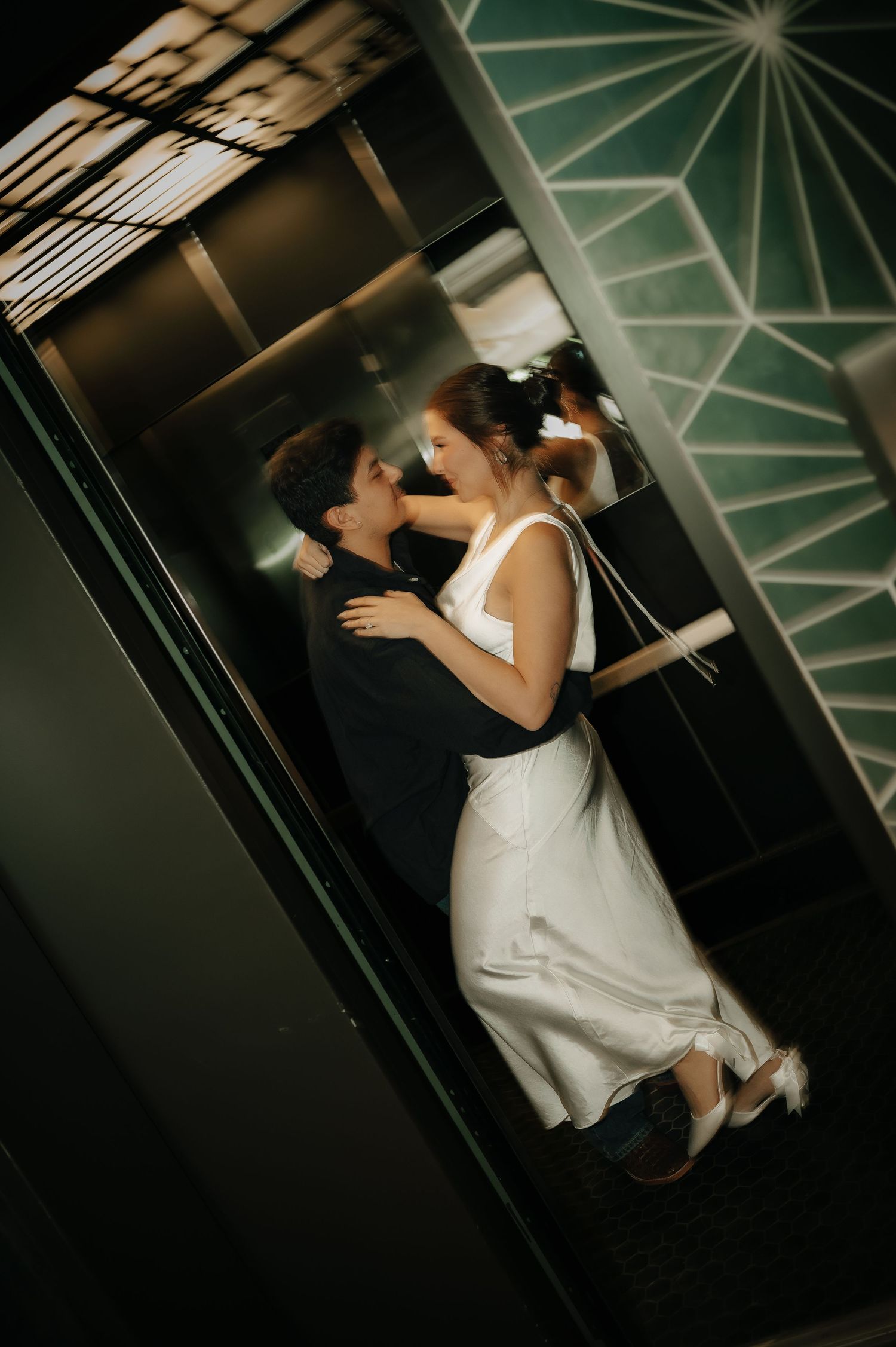 A couple embraces in a modern hallway with geometric patterns on the ceiling.
