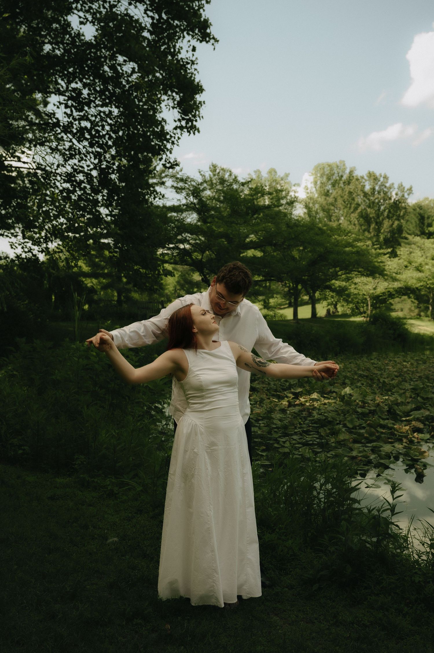 A bride and groom dance together outdoors in a lush green garden setting on their wedding day.