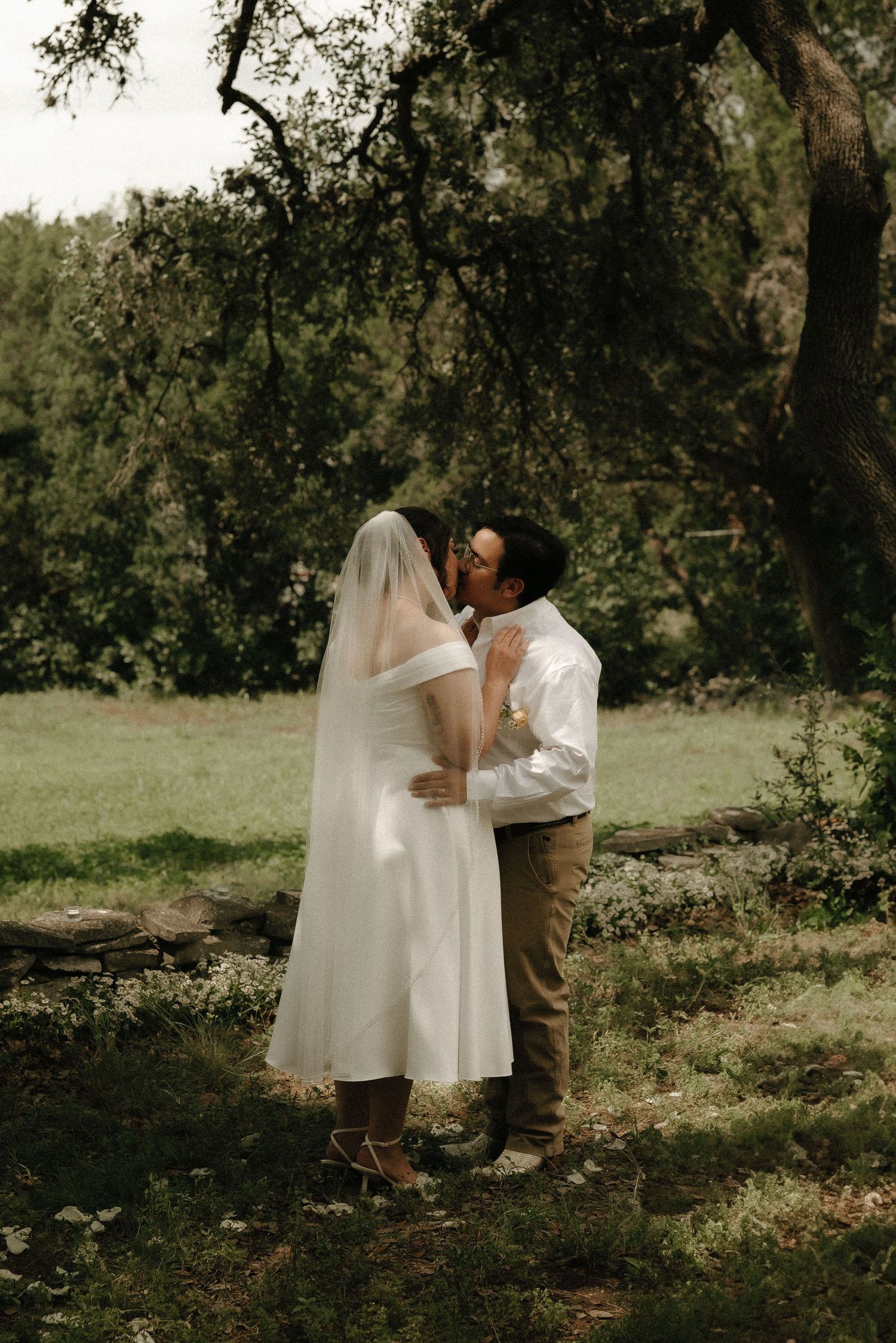 A romantic wedding ceremony moment captured in a natural outdoor setting with trees.