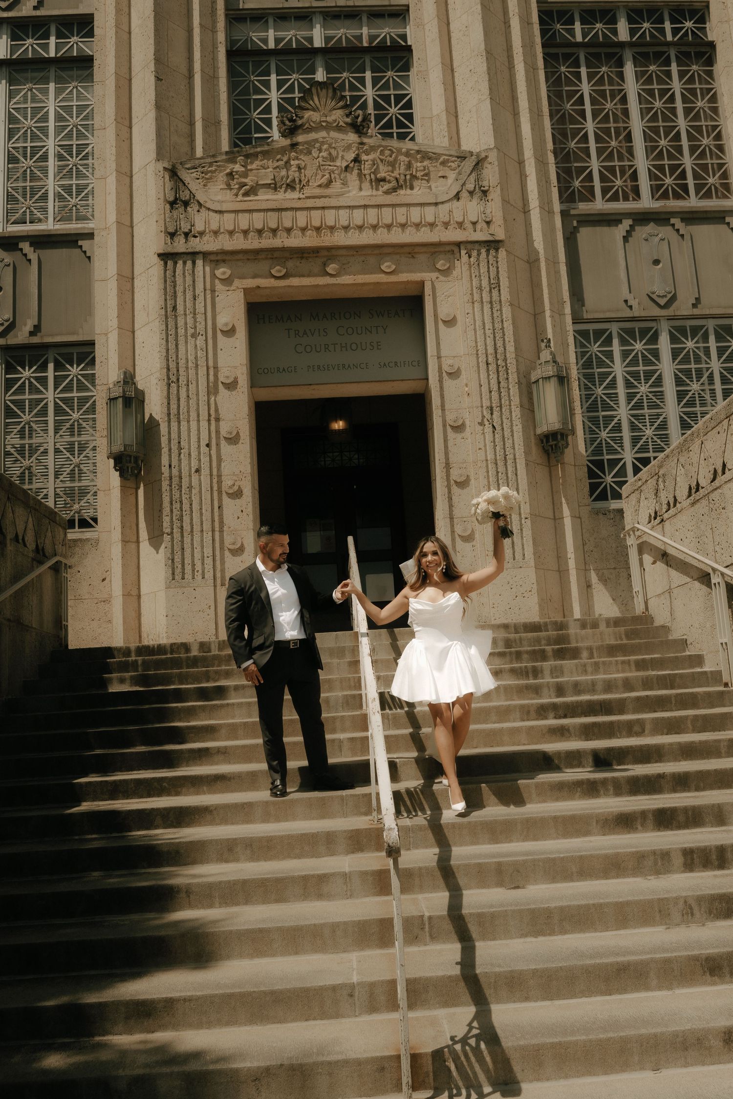 A newlywed couple celebrates joyfully on stone steps of a historic building.