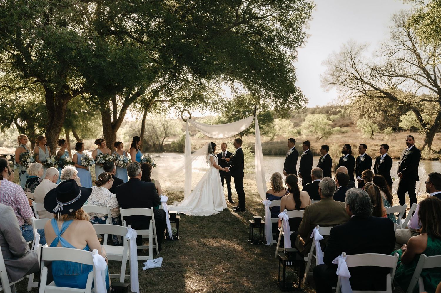 Outdoor wedding ceremony setup with white chairs and natural backdrop.