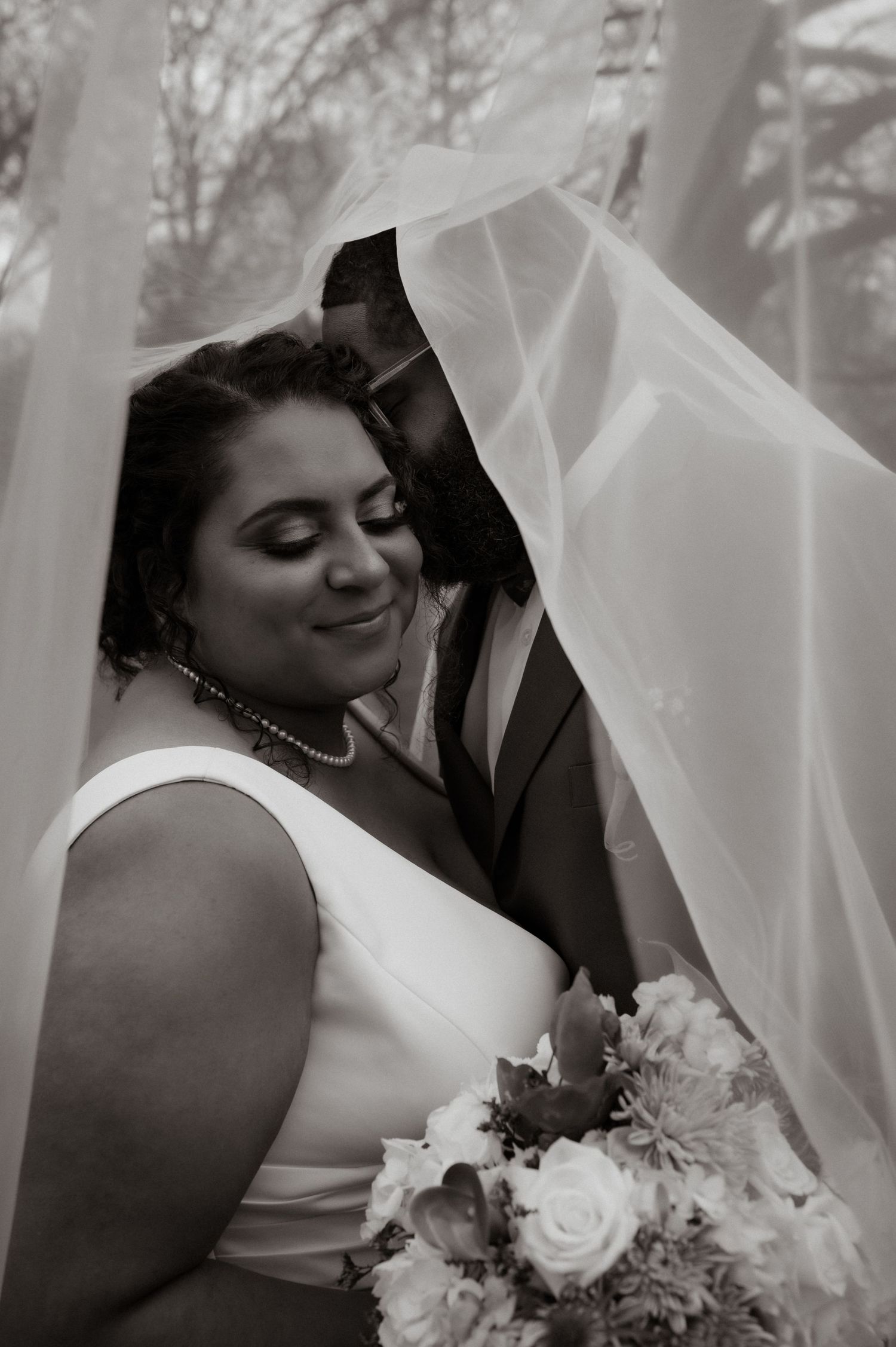Romantic wedding portrait through flowing white veil with white rose bouquet.
