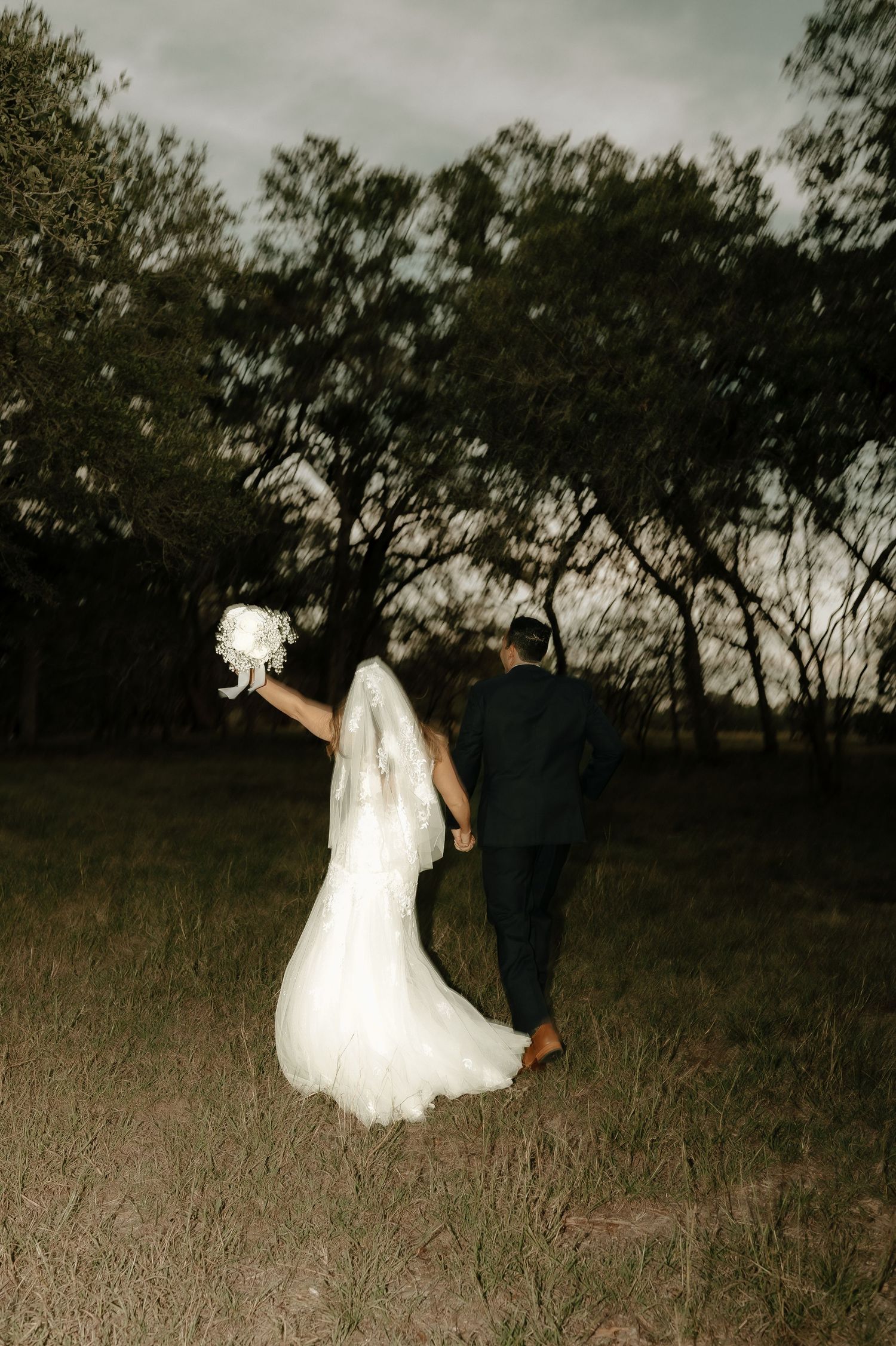 Romantic wedding couple dancing and twirling in a field during dusk.