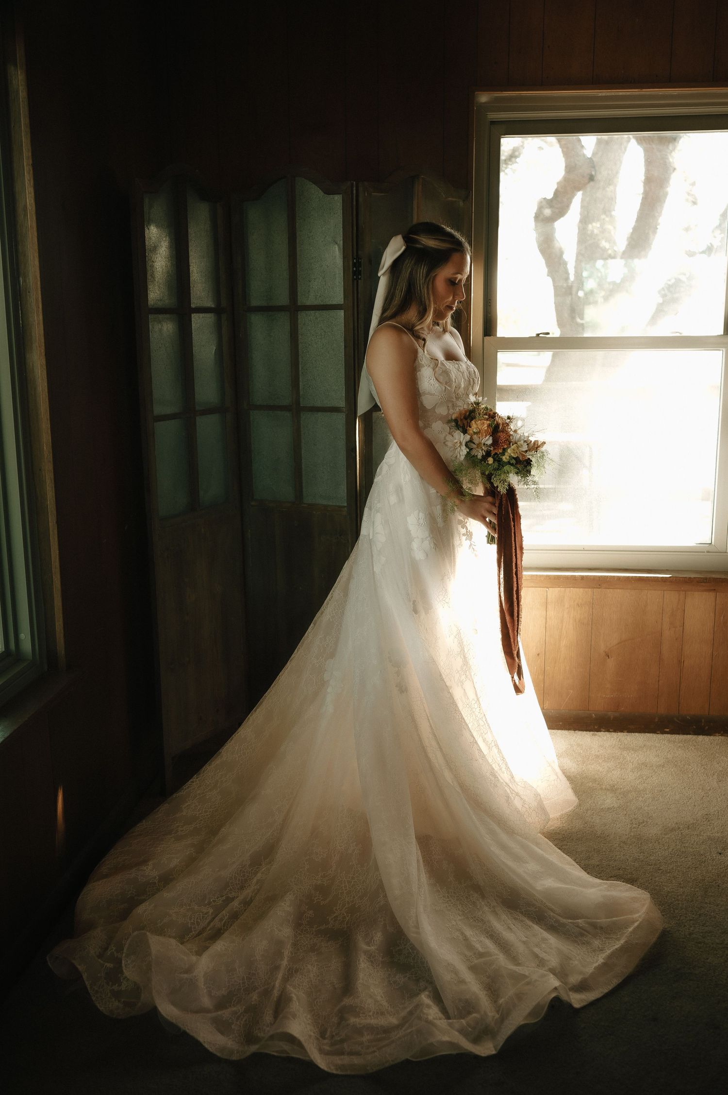 Elegant wedding dress with flowing train captured in dramatic window lighting.