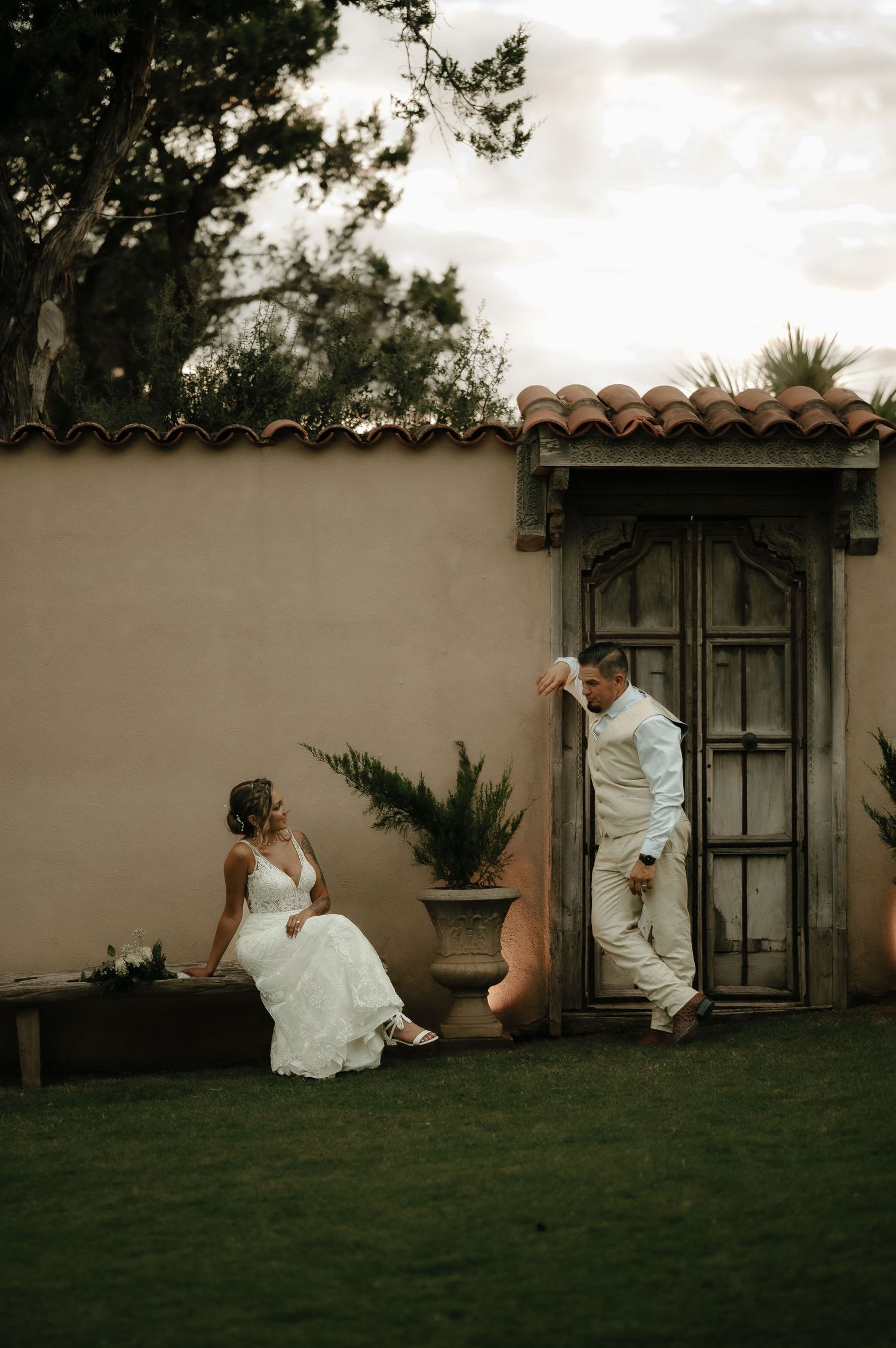 Couple sitting casually against a white stucco wall in a garden setting.