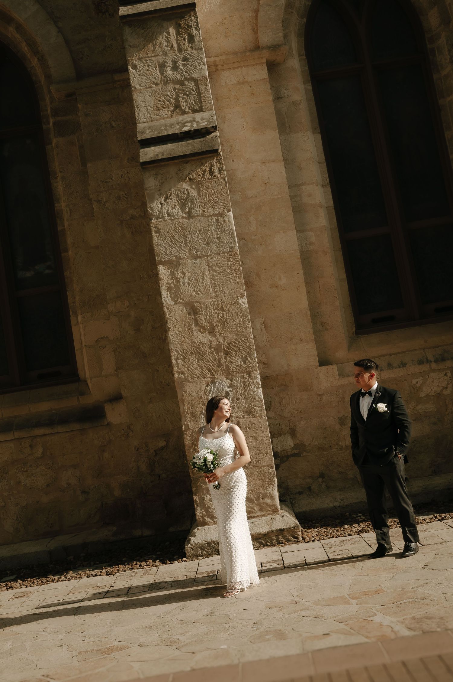 A couple stands against stone architecture in formal wedding attire.