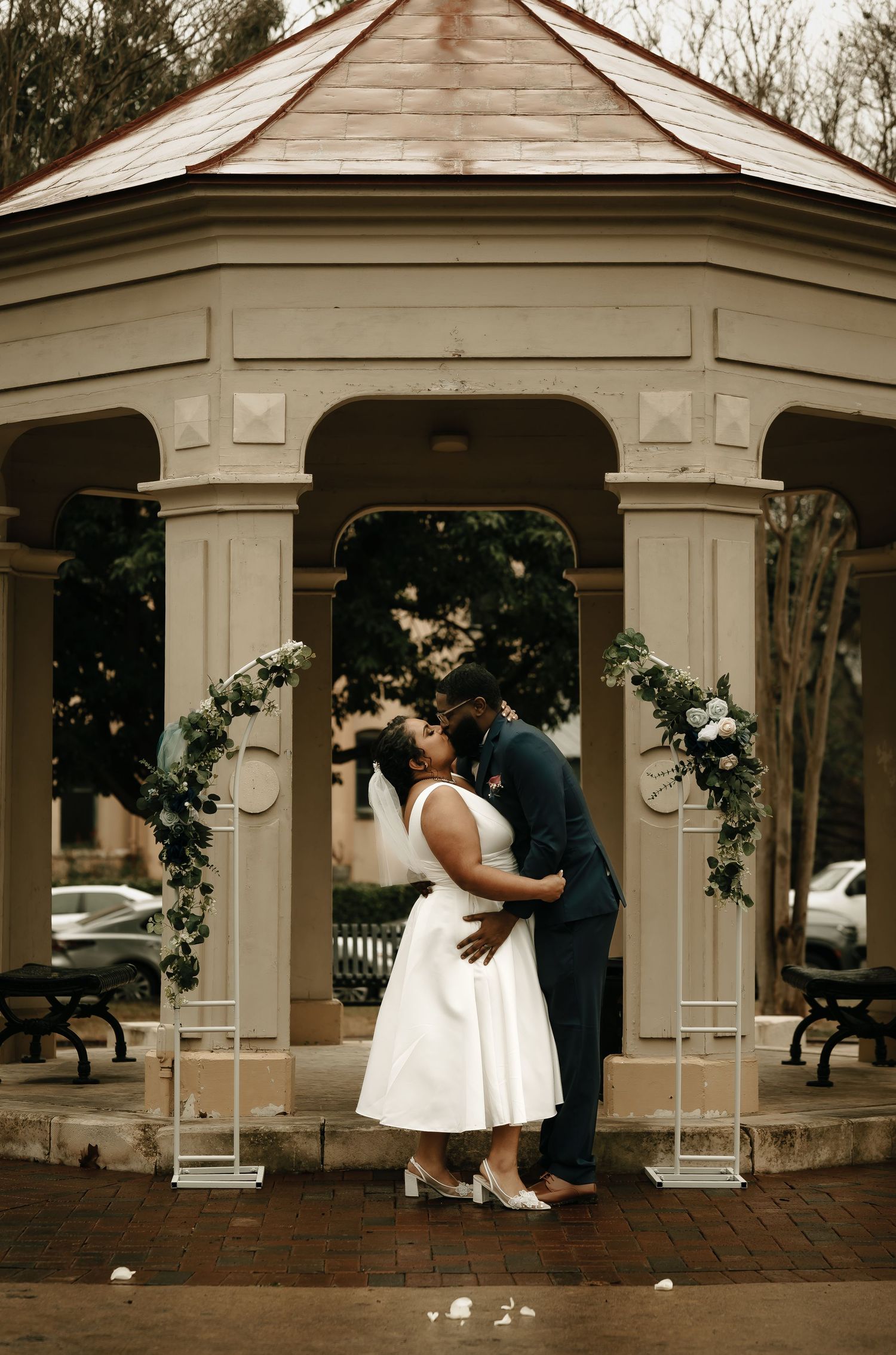Wedding couple sharing romantic moments under a white gazebo surrounded by trees.