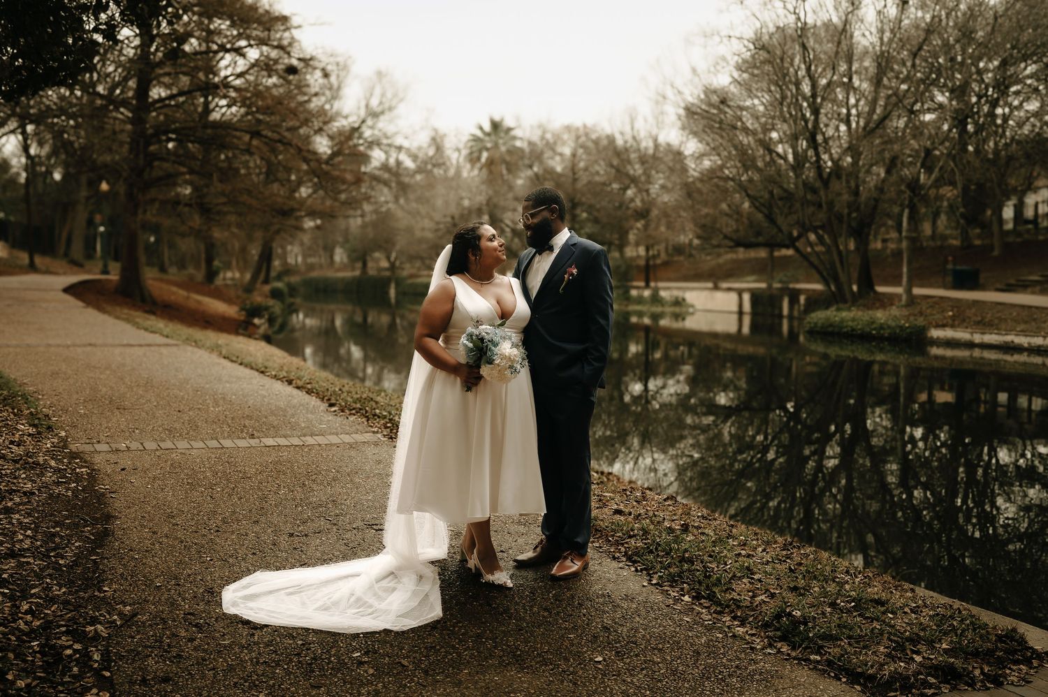 Romantic wedding couple poses in a park during autumn with fallen leaves on the ground.