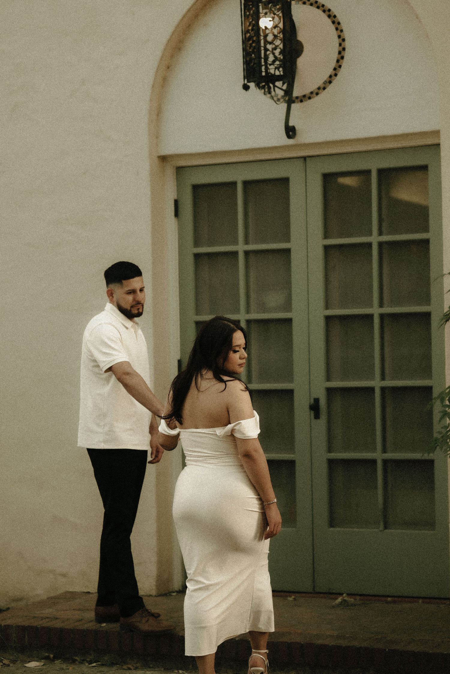 Artistic engagement photos showing intimate poses against a cream-colored architectural backdrop.