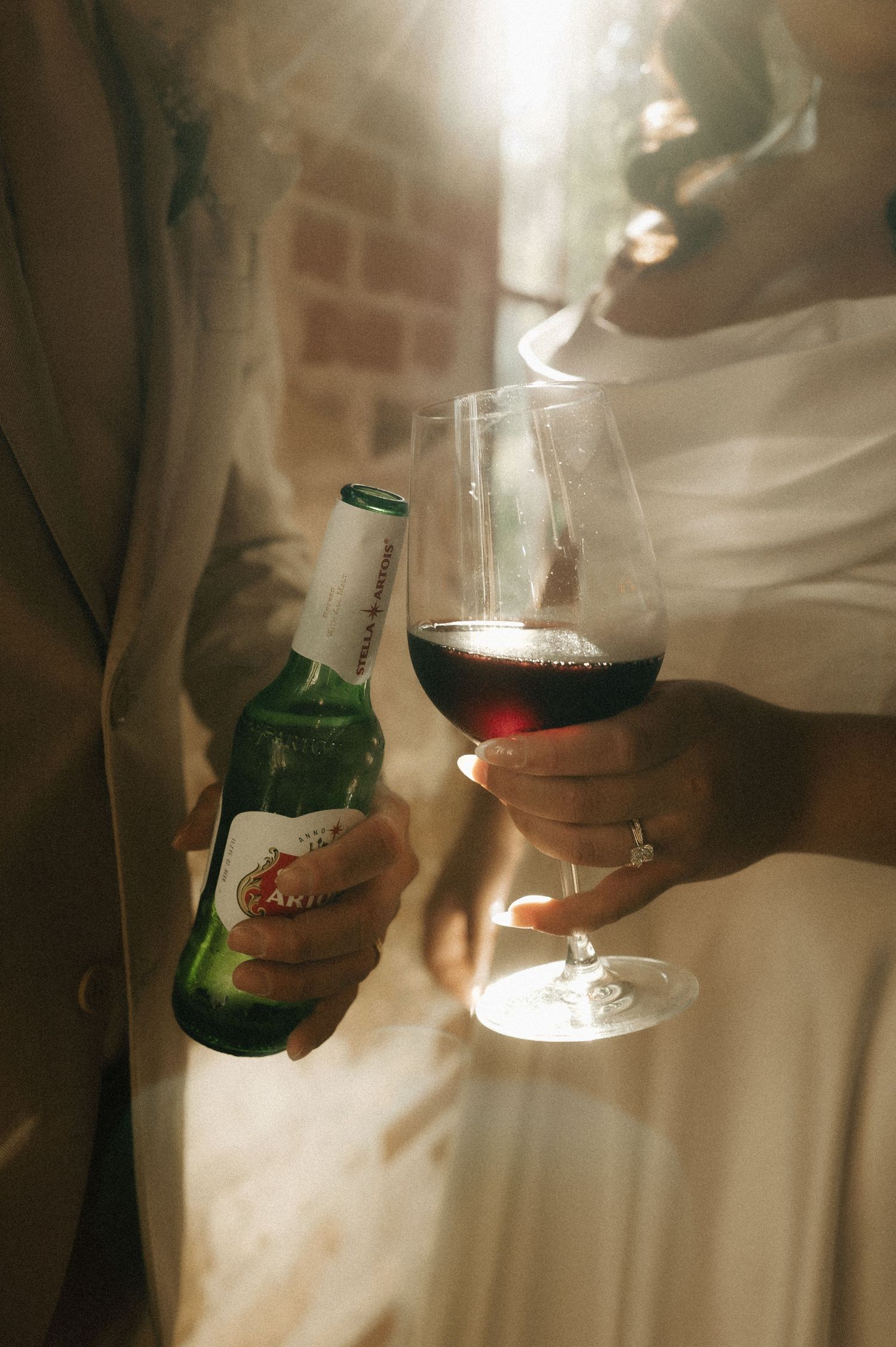Hands holding wine glasses and beer bottles at a wedding celebration.