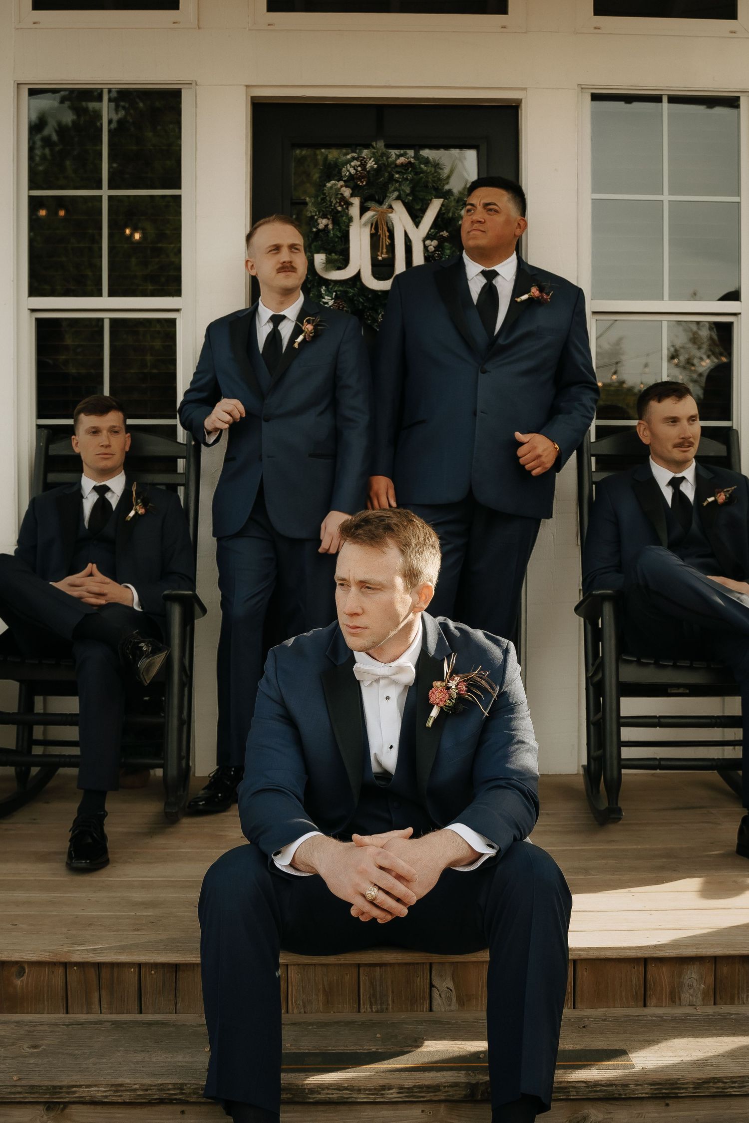 Groomsmen in navy suits relaxing on white porch steps.