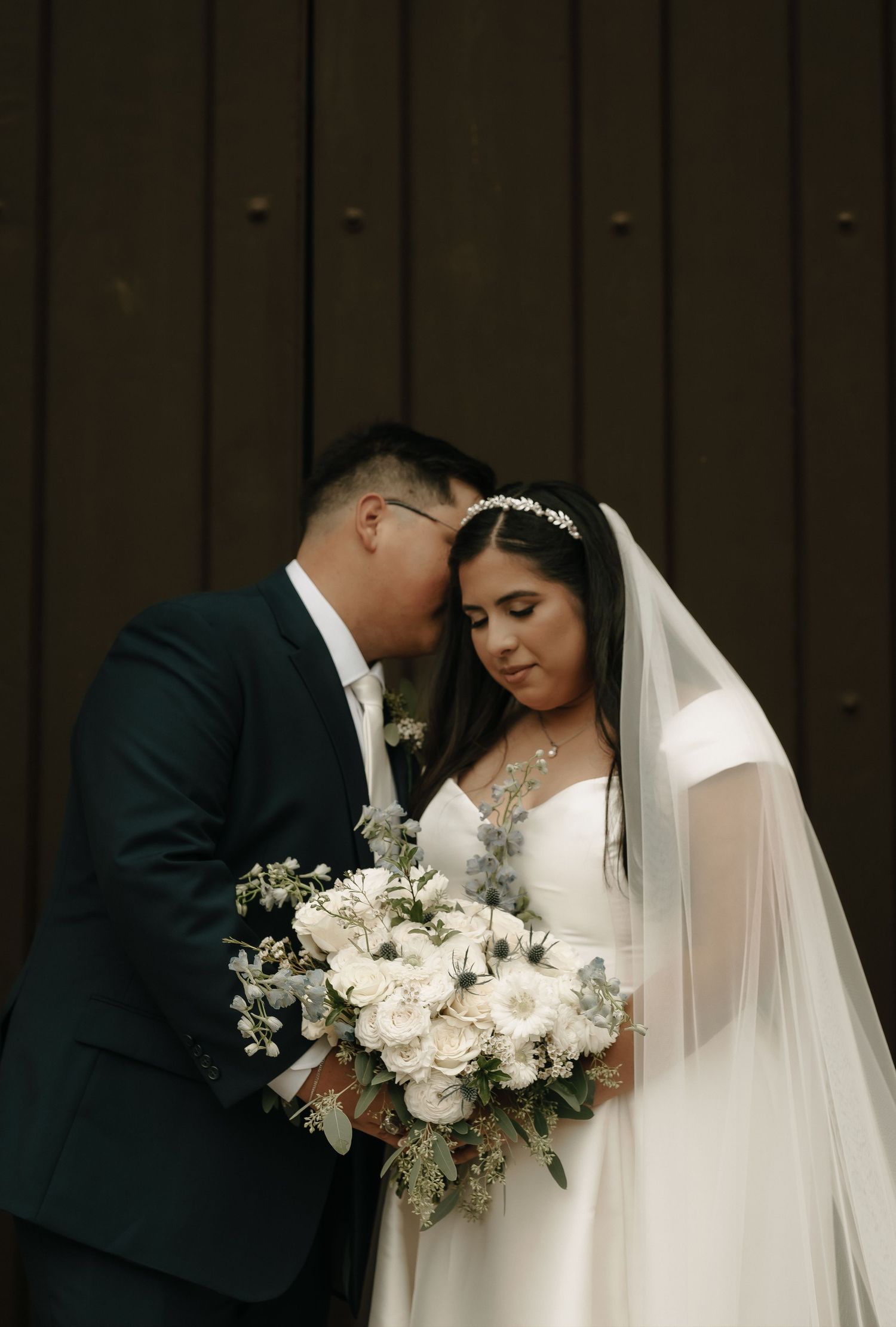 Intimate wedding portrait with white floral bouquet against dark wall.
