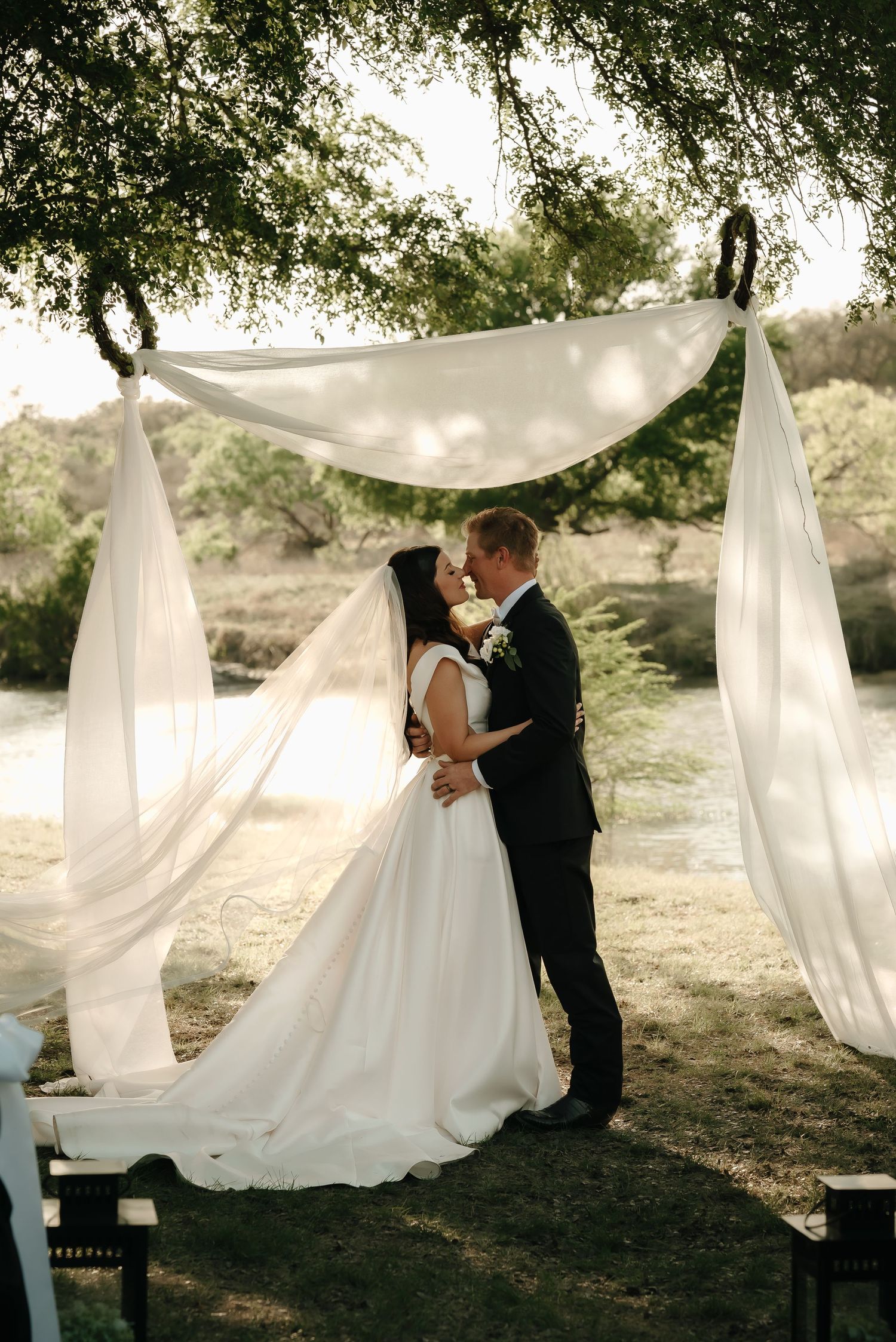 Elegant outdoor wedding scene with flowing white drapery hanging between trees.
