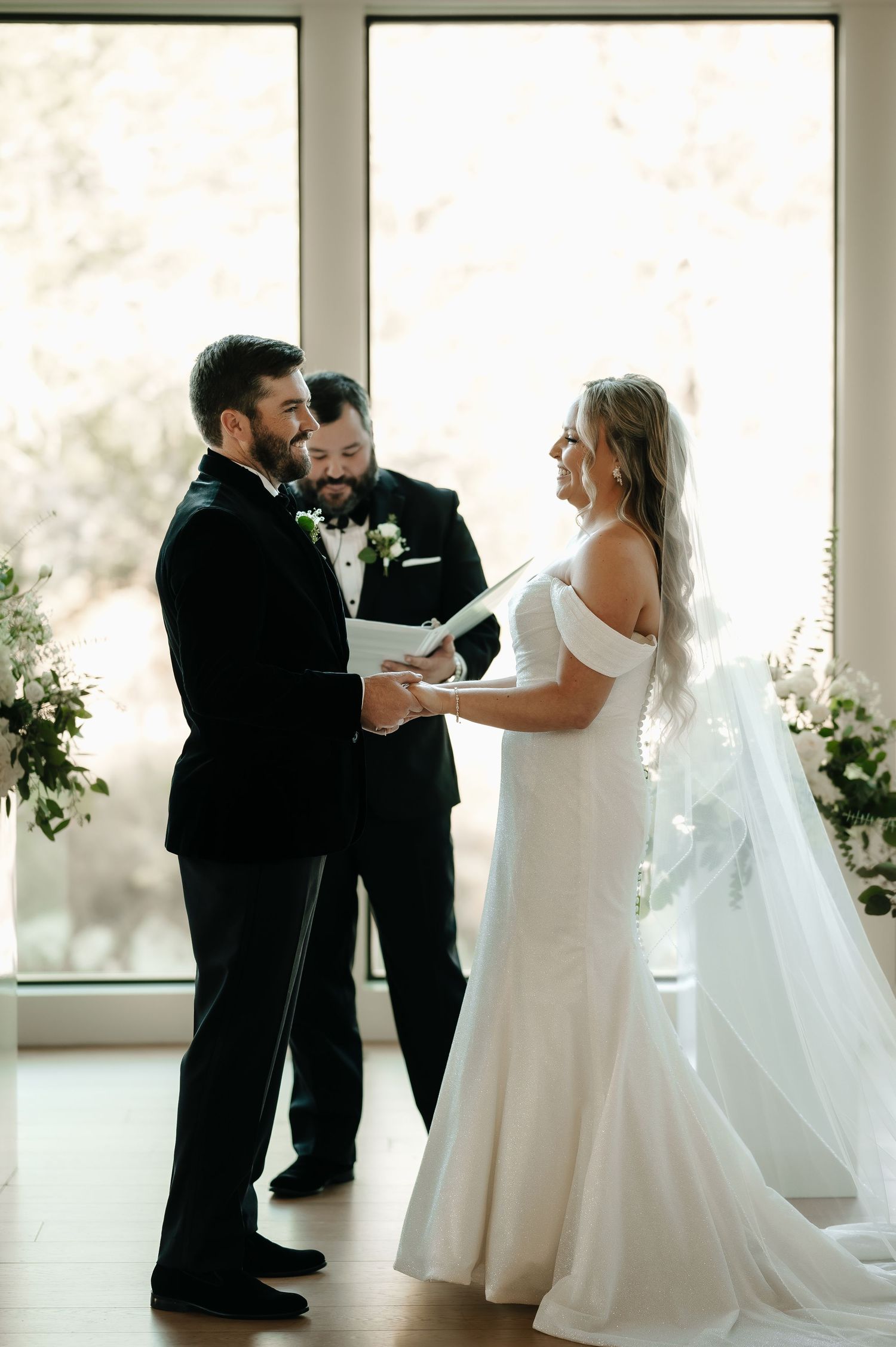 A romantic first look moment between newlyweds in an elegant white venue with floor-to-ceiling windows.