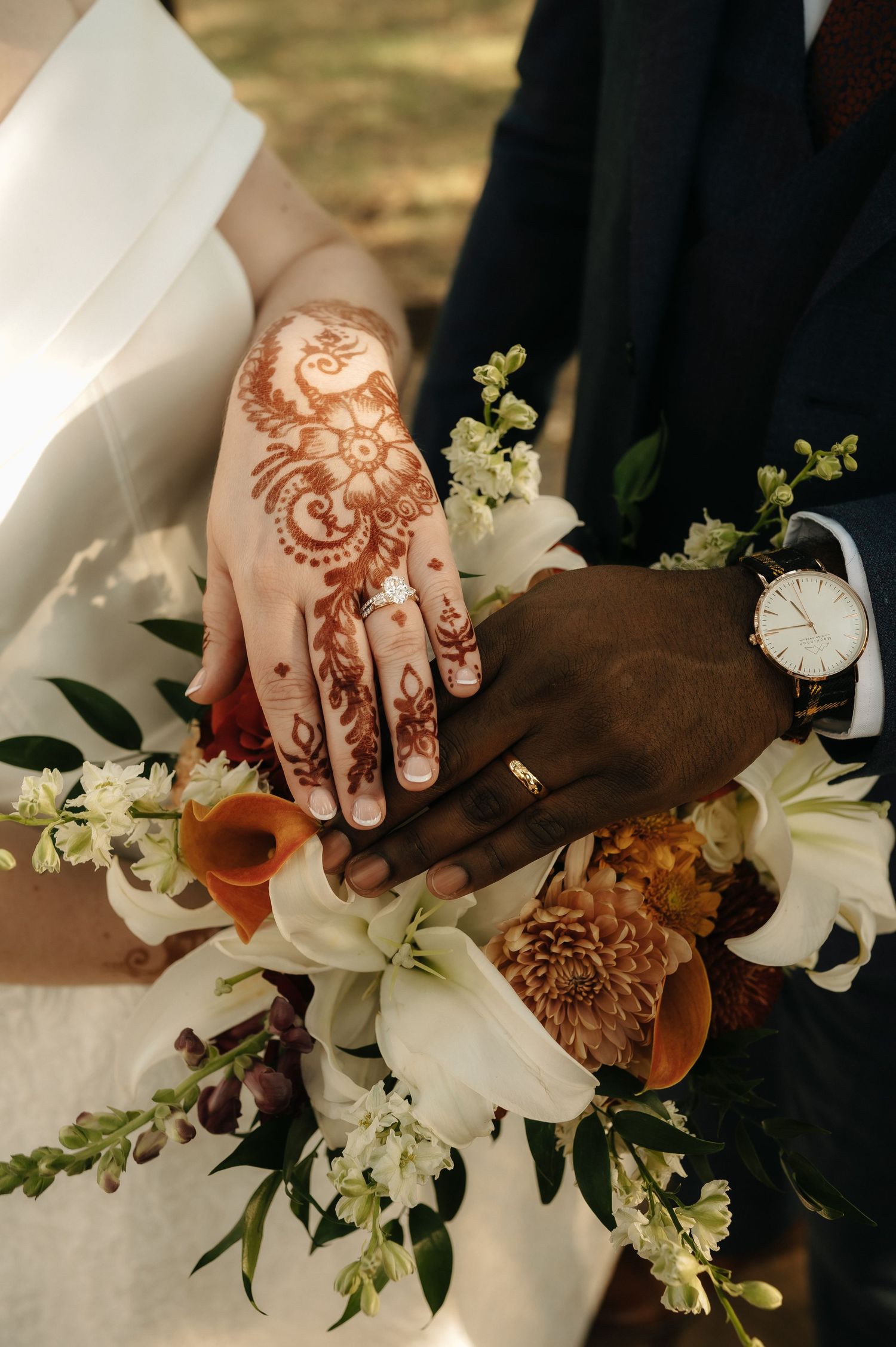 Close-up of intricate henna designs on hands holding white and orange floral bouquet.