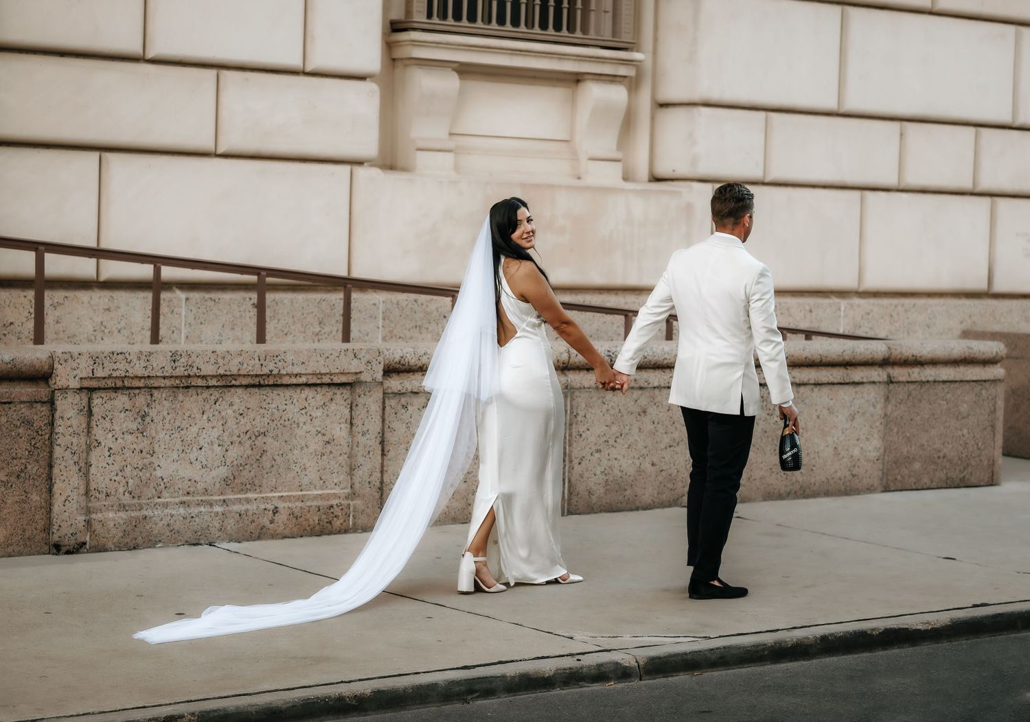 Wedding photoshoot along an elegant stone building exterior.