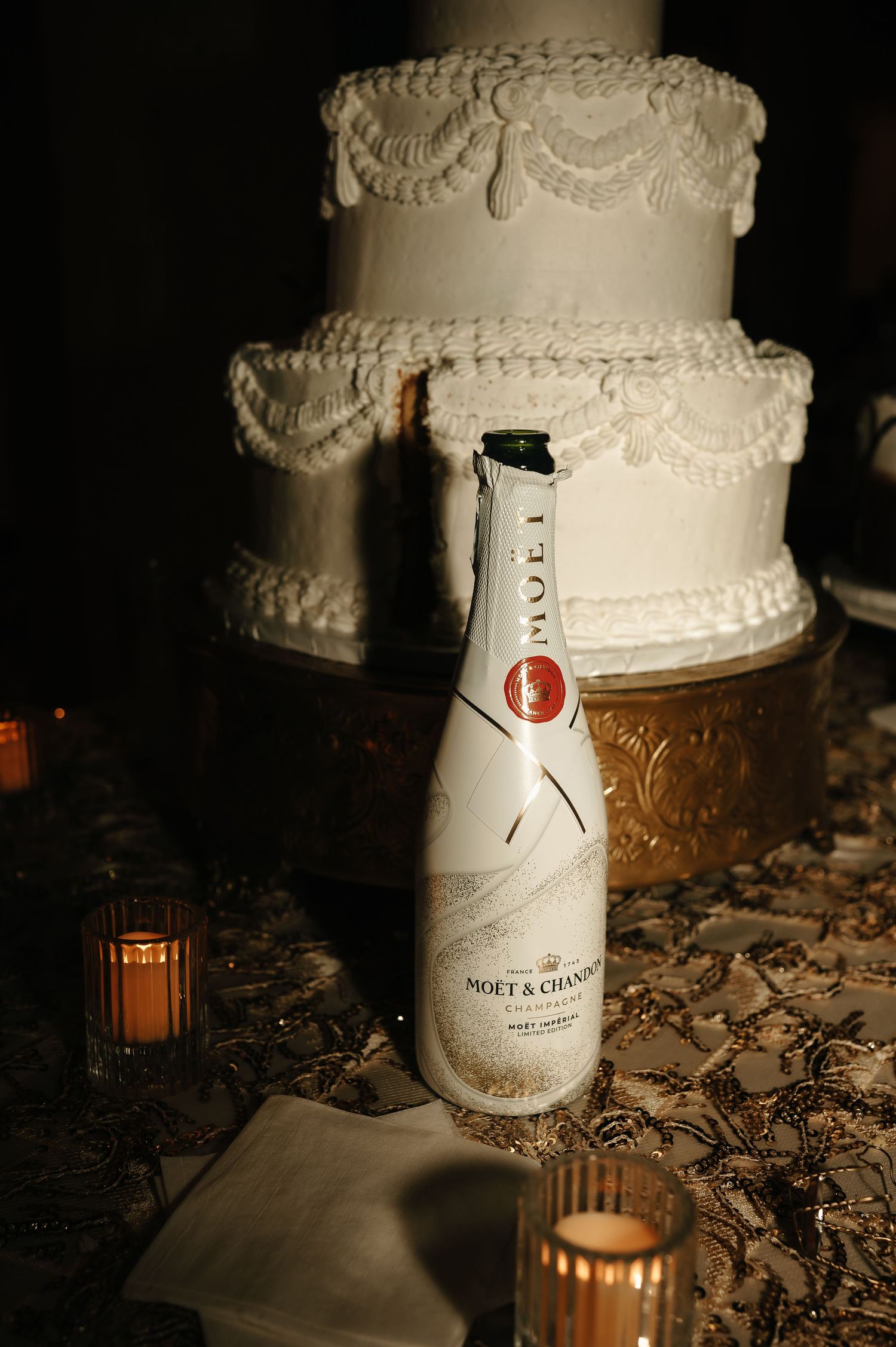 Elegant white wedding cake displayed with Moët & Chandon champagne bottle and candlelight.