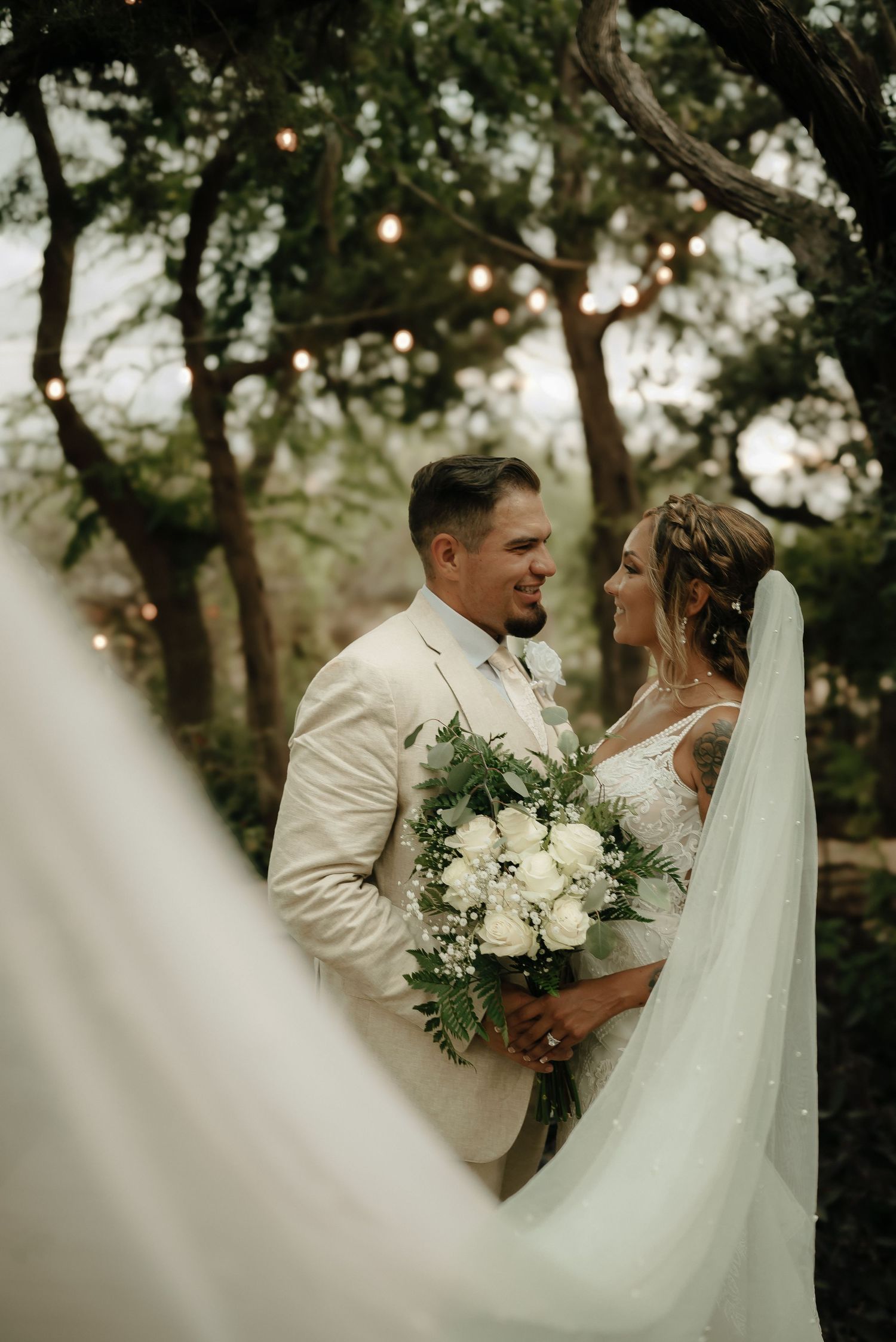 Romantic outdoor wedding scene with flowing white dress and lush greenery in the background.
