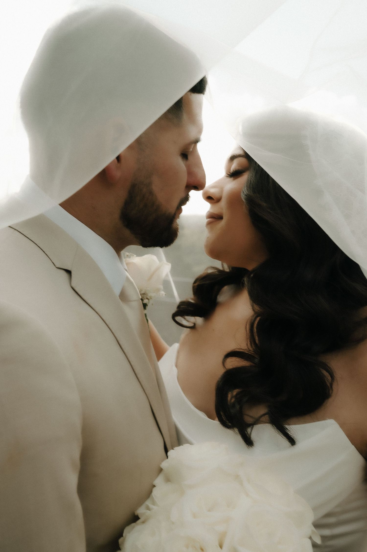 A couple in white wedding attire shares an intimate moment against a bright background.