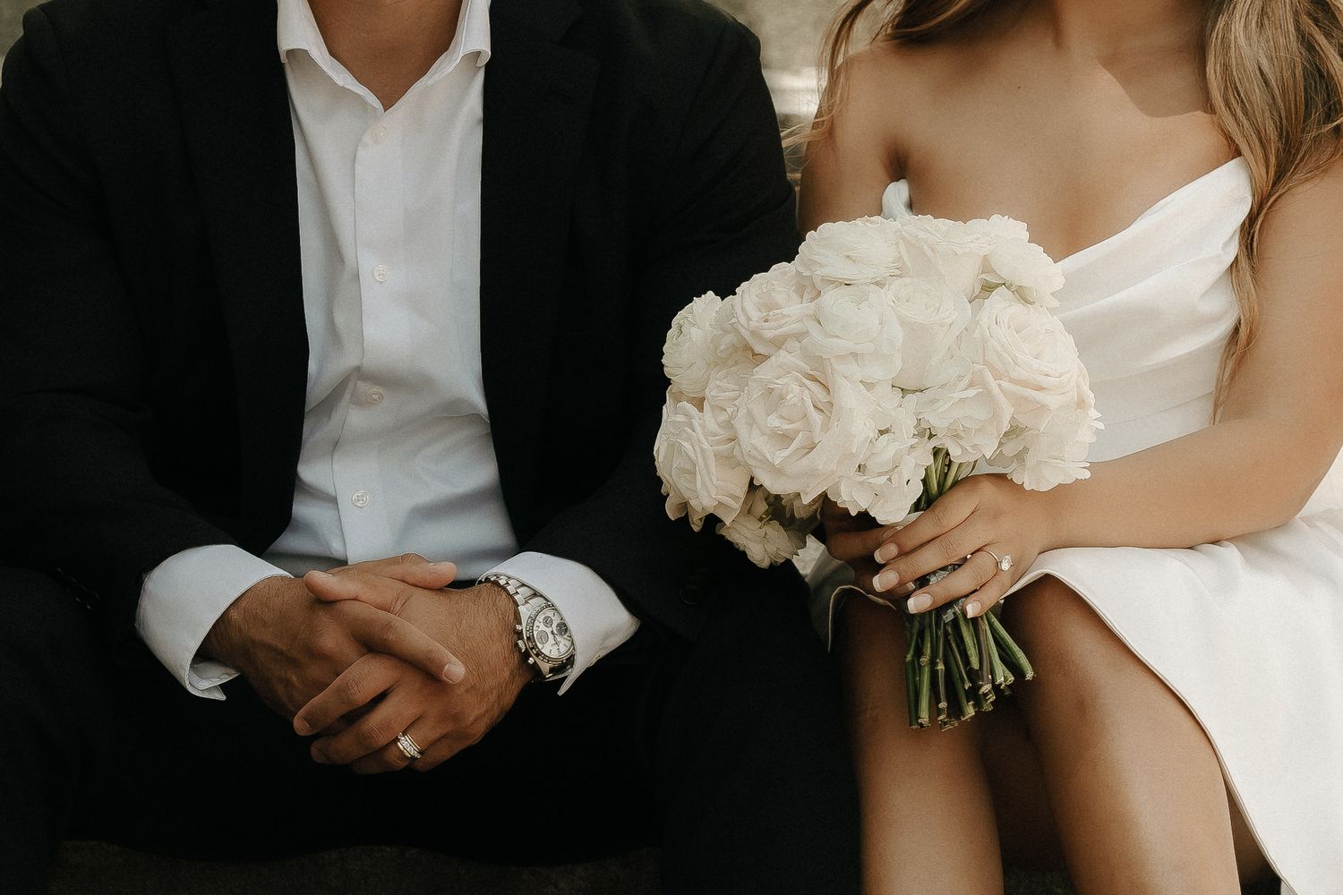 A close-up wedding photo showing formal attire and white rose bouquet.