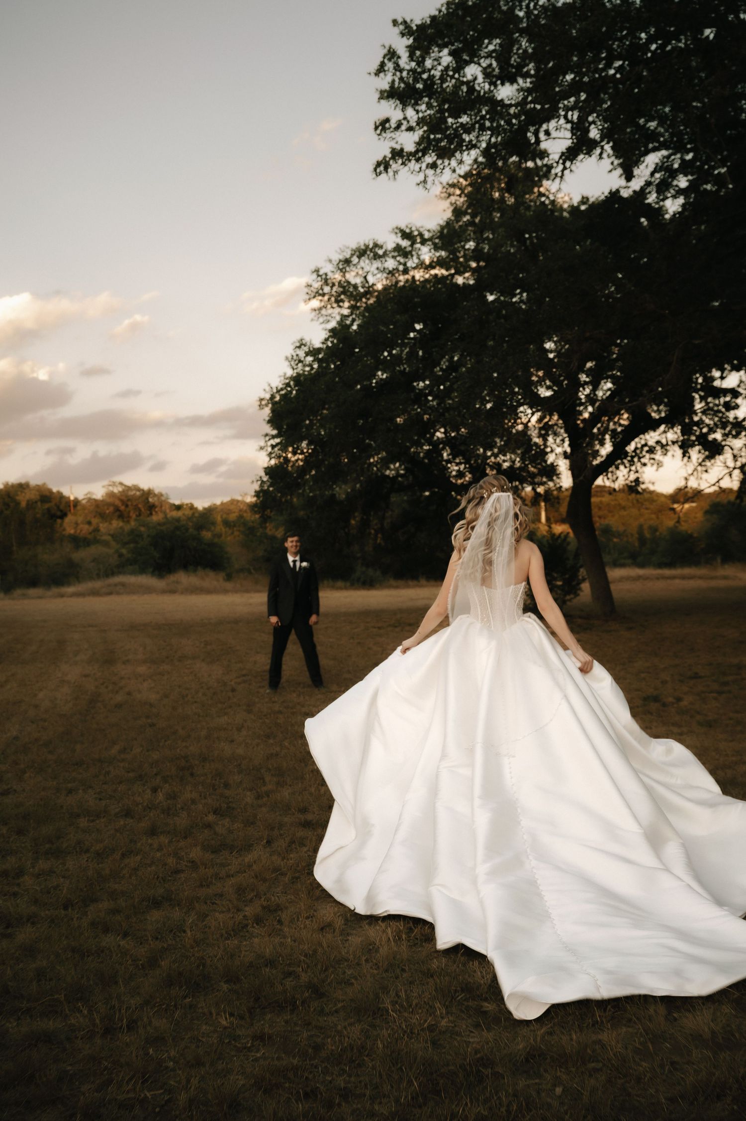 Dramatic sunset photo of bride in flowing dress with groom in distance.