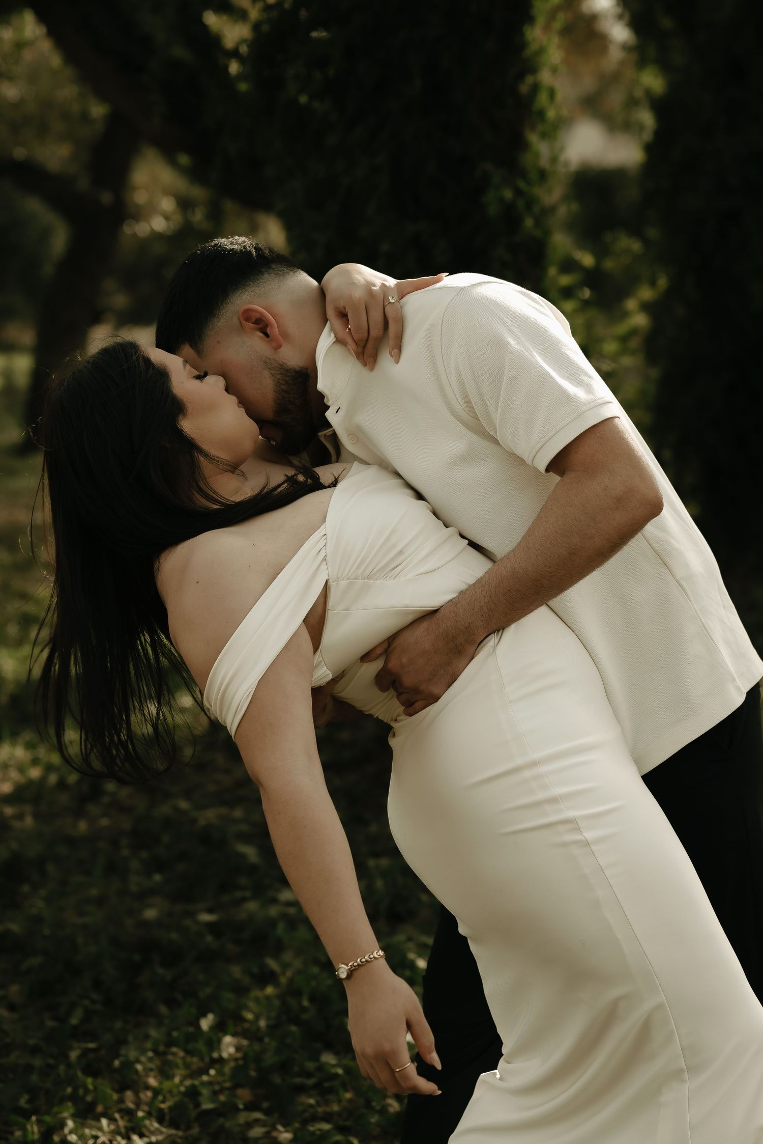 An intimate dance pose between a couple wearing white clothing in a wooded setting.