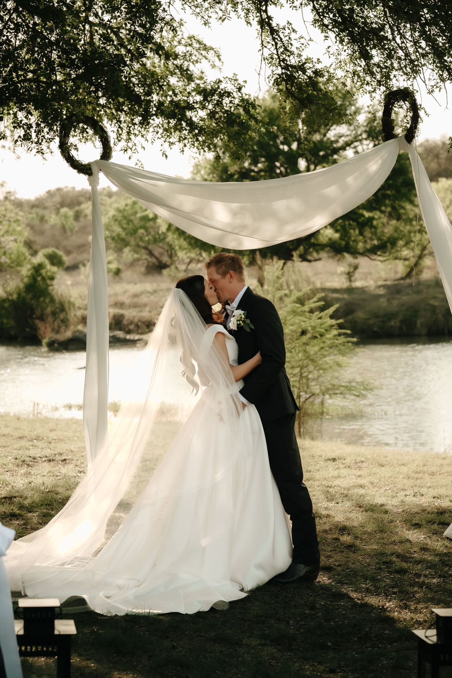 Romantic wedding photoshoot by a lake with flowing white dress and elegant draping.