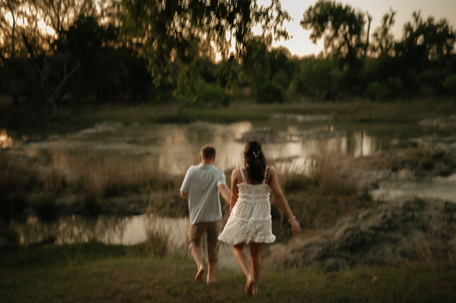 Silhouettes walking together at sunset near a reflective pond.