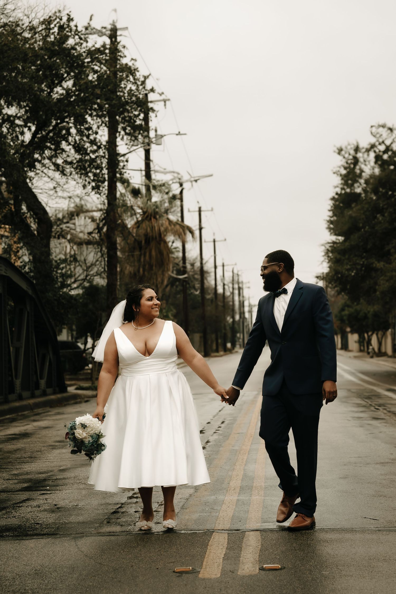 Couple walks hand in hand on city street in wedding attire.