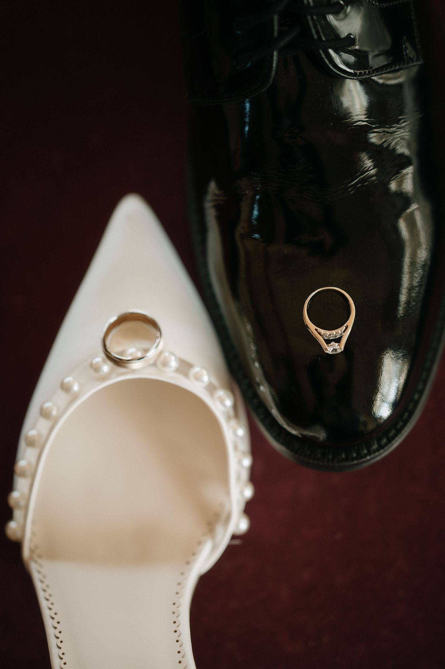 Wedding rings artistically placed on white bridal shoe and black formal shoe.