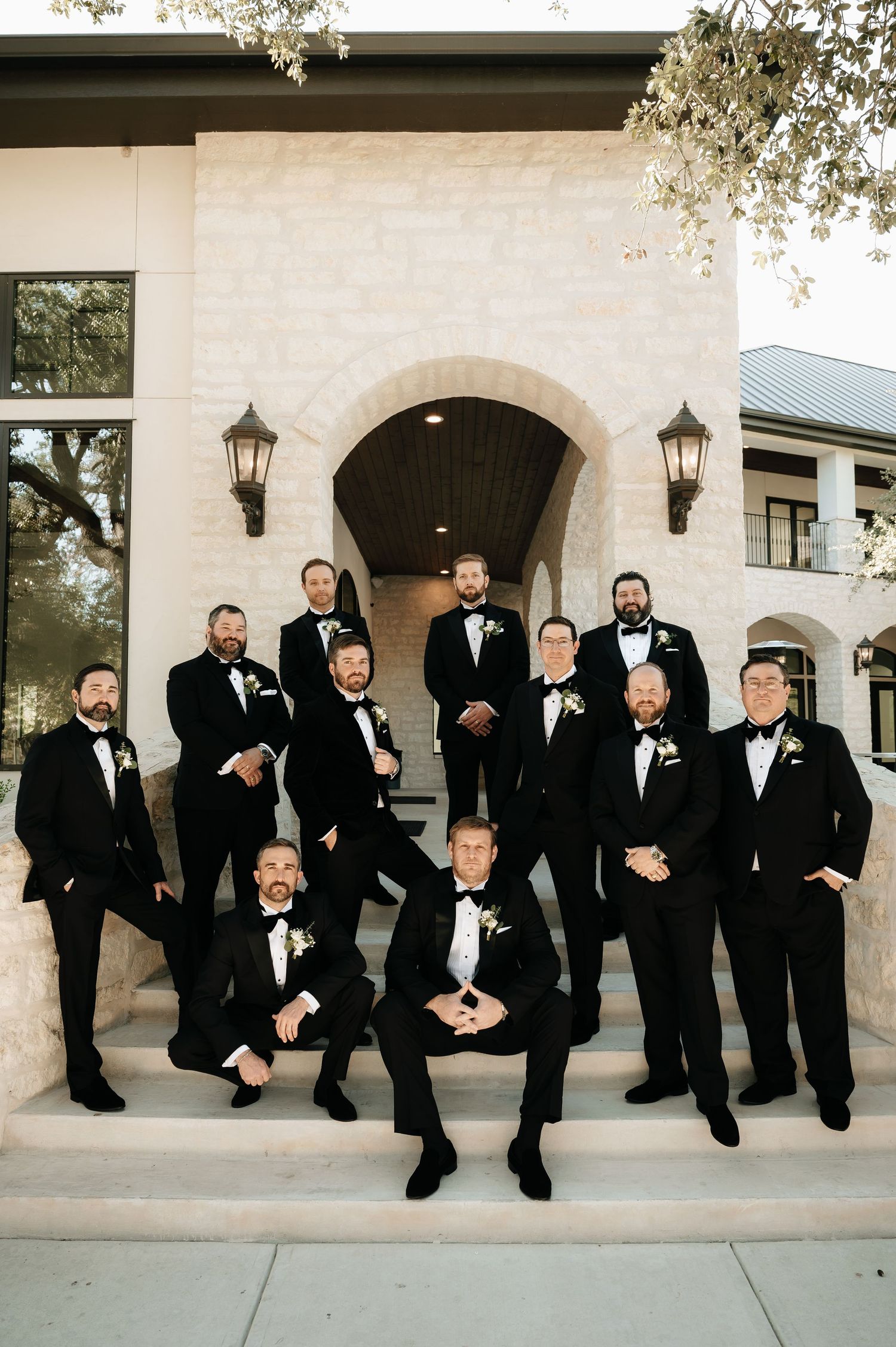 Groomsmen in classic black tuxedos posed casually on stone steps.