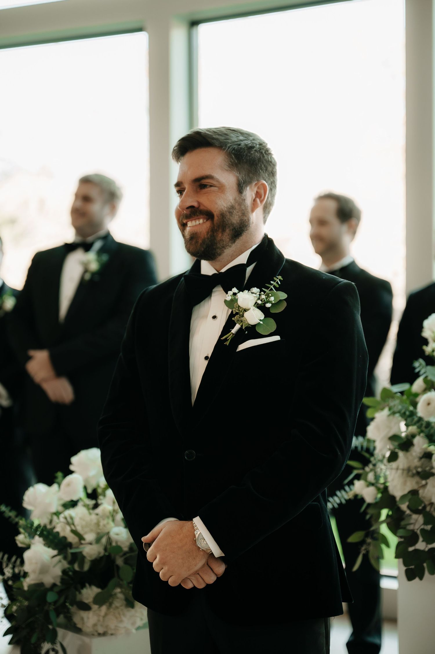 Formal wedding gathering in a bright indoor venue decorated with white flowers.