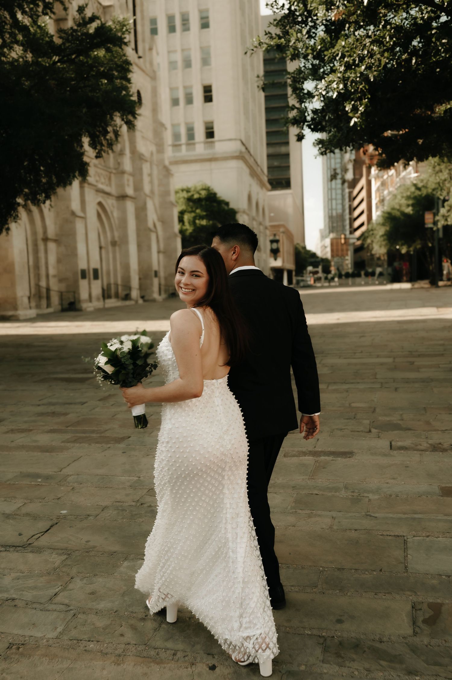 Couple dances playfully on stone steps in urban wedding setting.