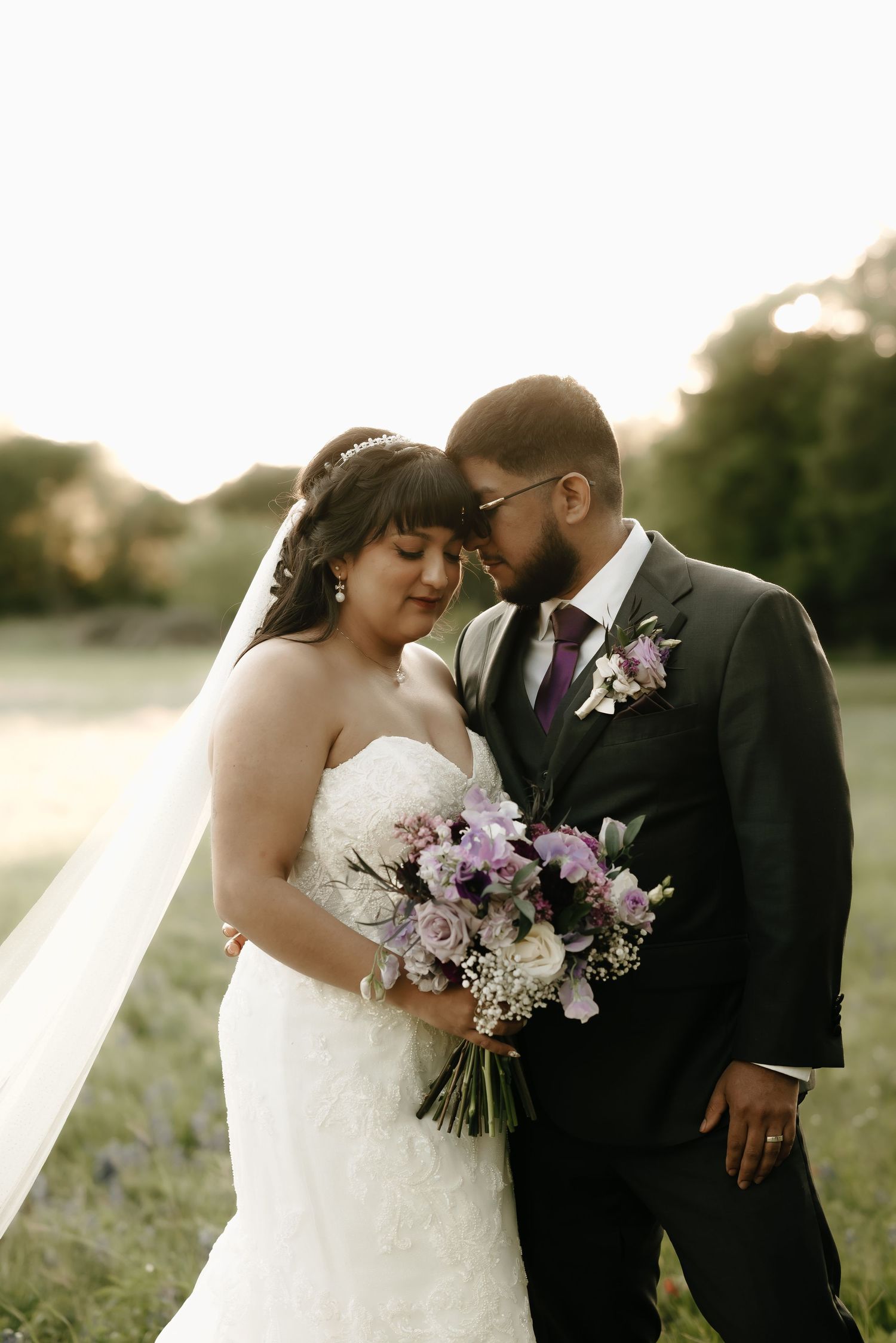 Intimate wedding portrait of couple with purple bouquet in golden evening light.