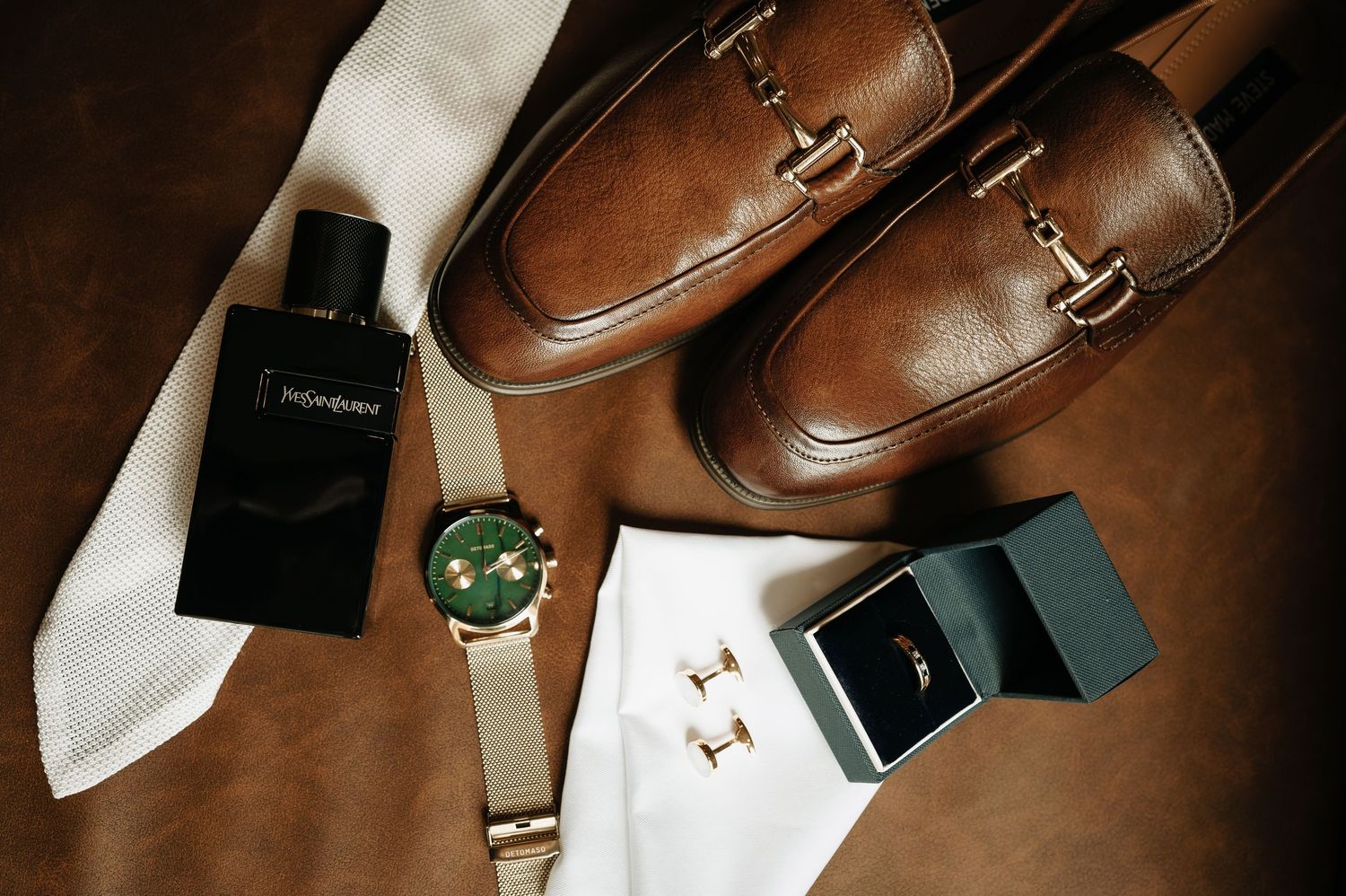 Wedding accessories including brown leather shoes and jewelry on dark background.