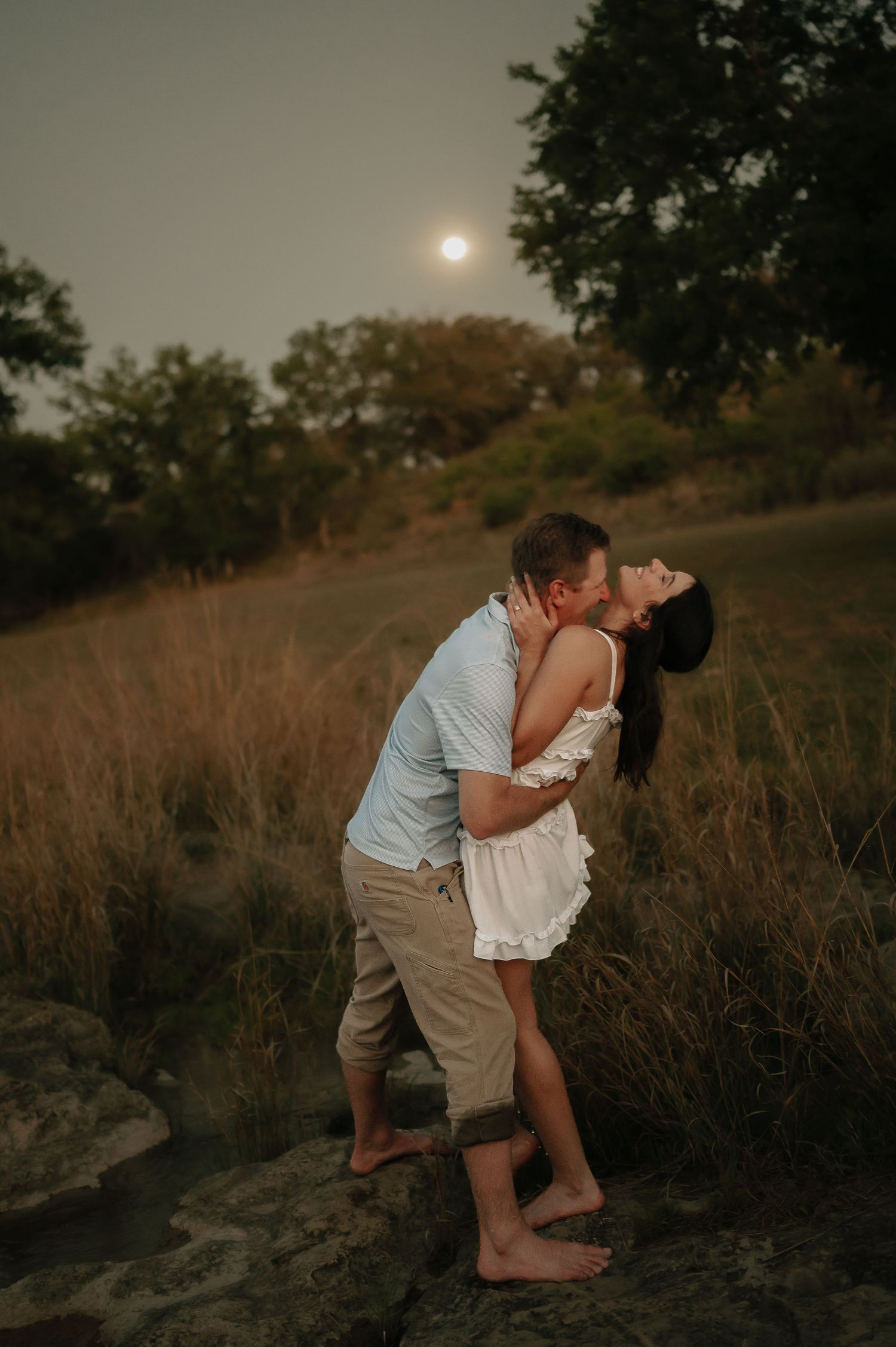 Romantic sunset embrace on a hilltop with golden light filtering through trees.