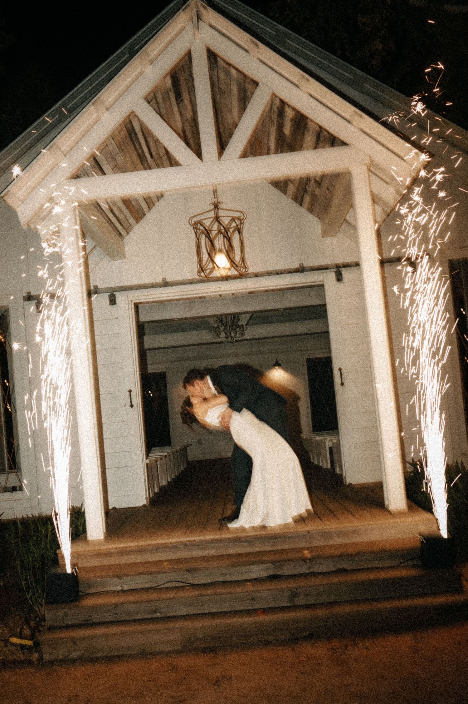 Dramatic wedding dance dip with sparkler effects in a rustic white barn venue.