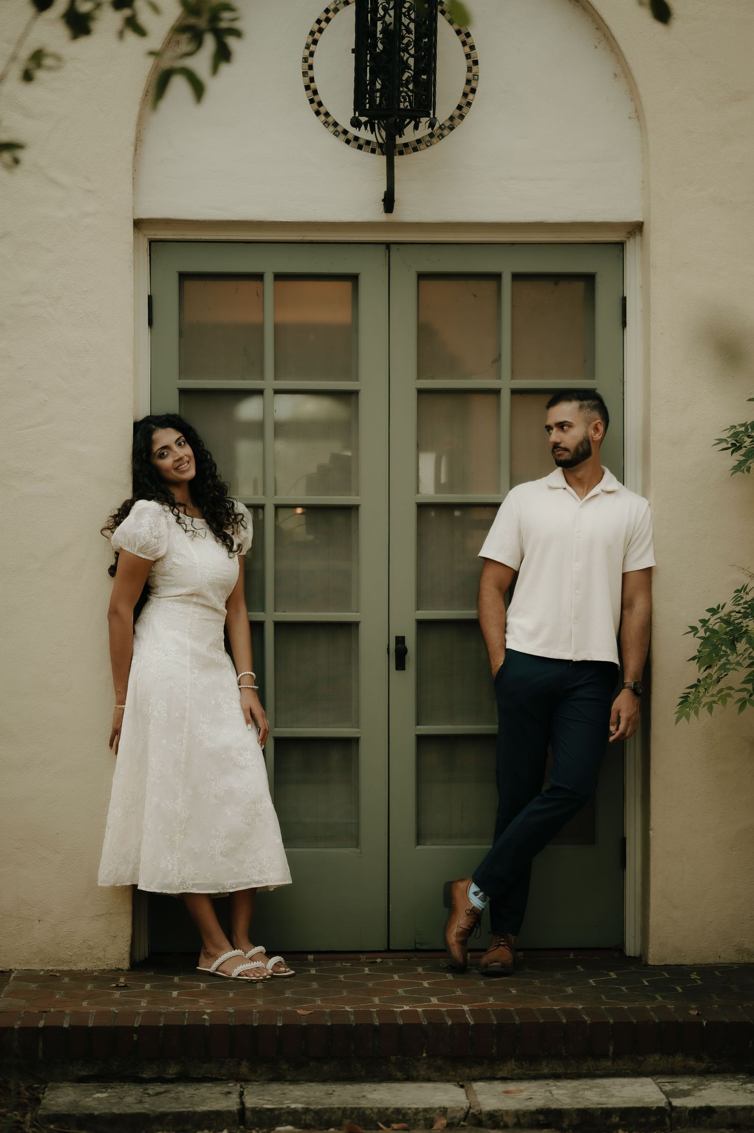 Stylish couple posing by vintage green doors in contrasting white and navy outfits.